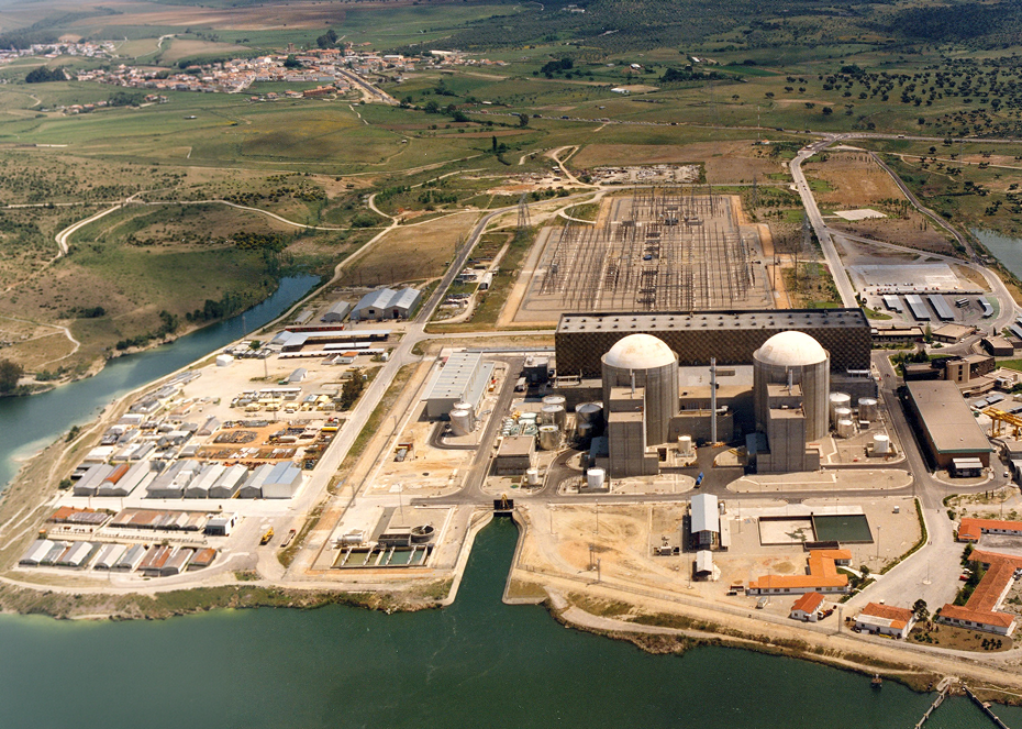 An aerial view of a nuclear power station beside a river, with containment towers and various industrial facilities surrounded by fields and hills.