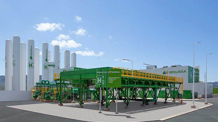 Iberdrola's green hydrogen production facility in Puertollano, featuring tall white storage tanks, green industrial structures, and H2 signage.
