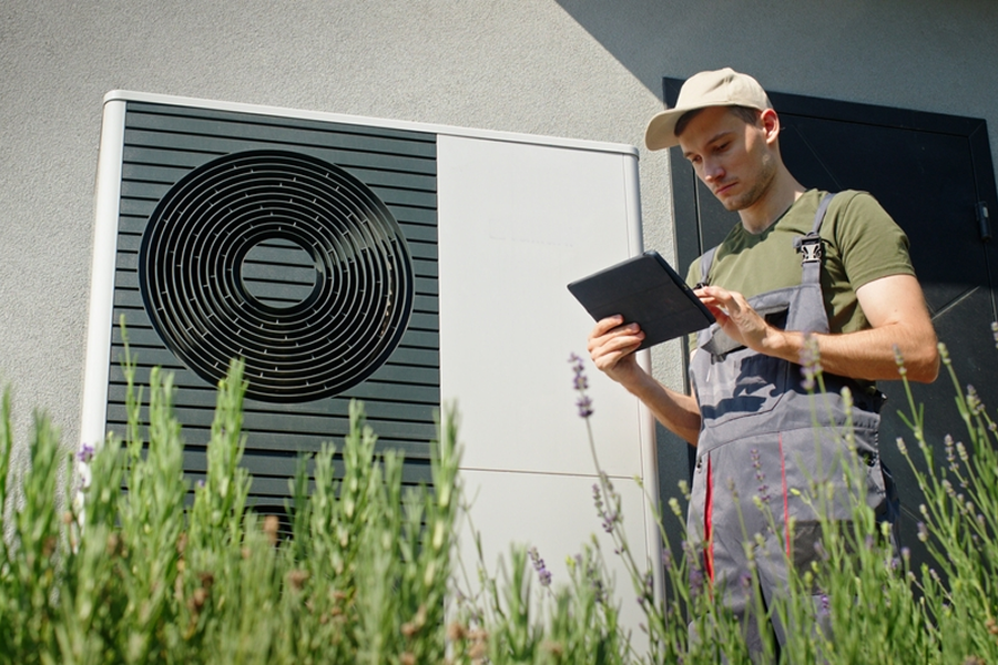 Técnico trabajando en la instalación de una unidad de energía, revisando información en una tablet frente a un sistema de aire acondicionado.