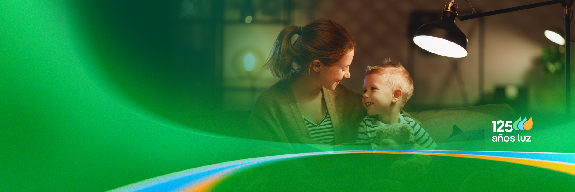 Una madre y su hijo se miran sonriendo, mientras una lámpara ilumina la escena en un ambiente cálido. Se destaca el logo de "125 años luz".