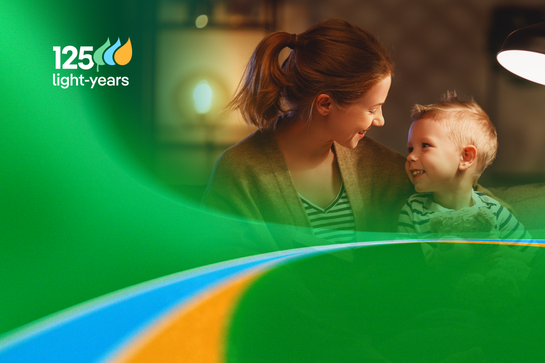 A mother and her son smile at each other, with a lamp illuminating the scene in a warm setting. The "125 years of light" logo is prominently displayed.