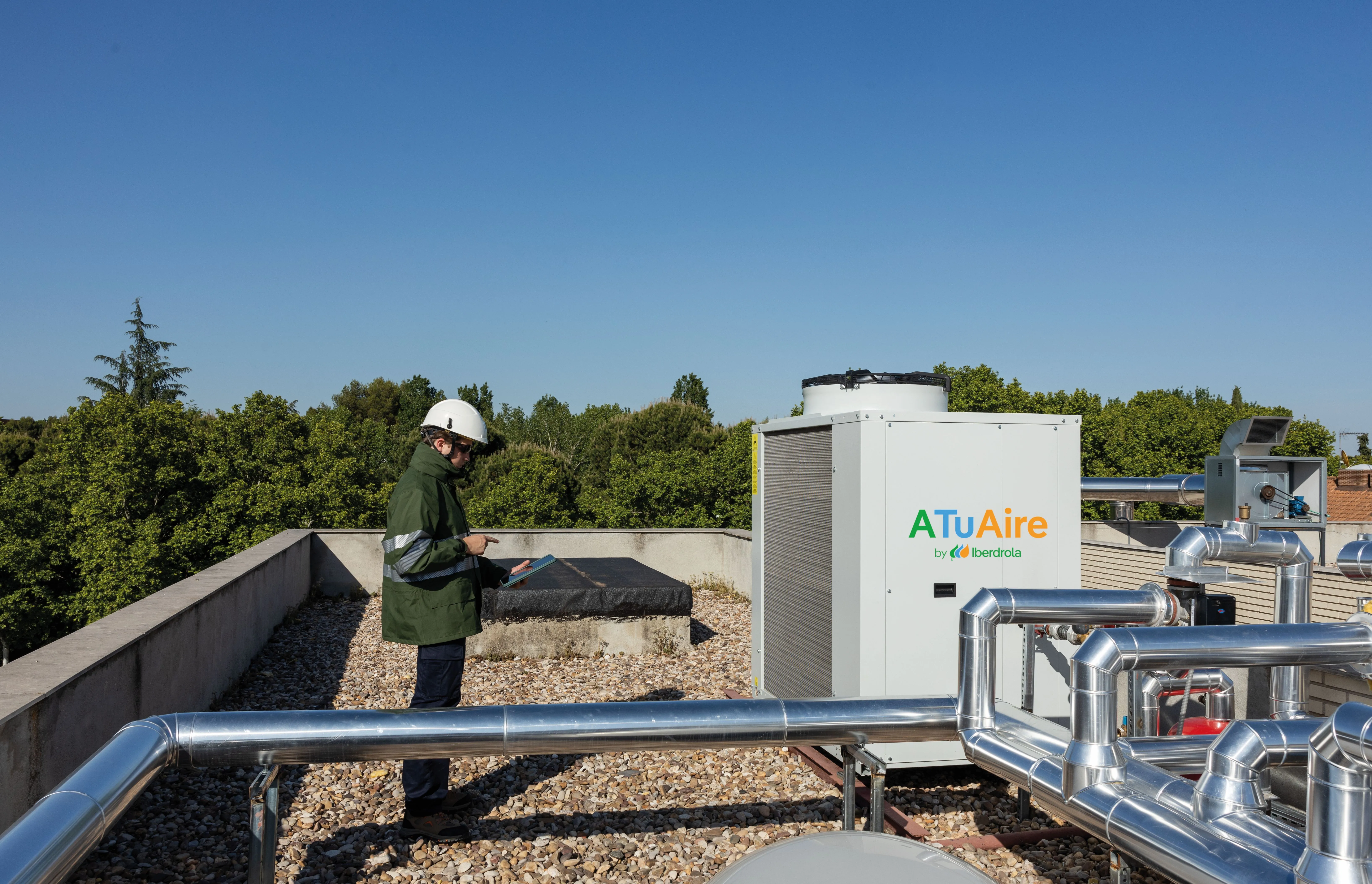 Técnico inspecciona un sistema de aerotermia en la cubierta de un edificio con equipos de climatización y tuberías.