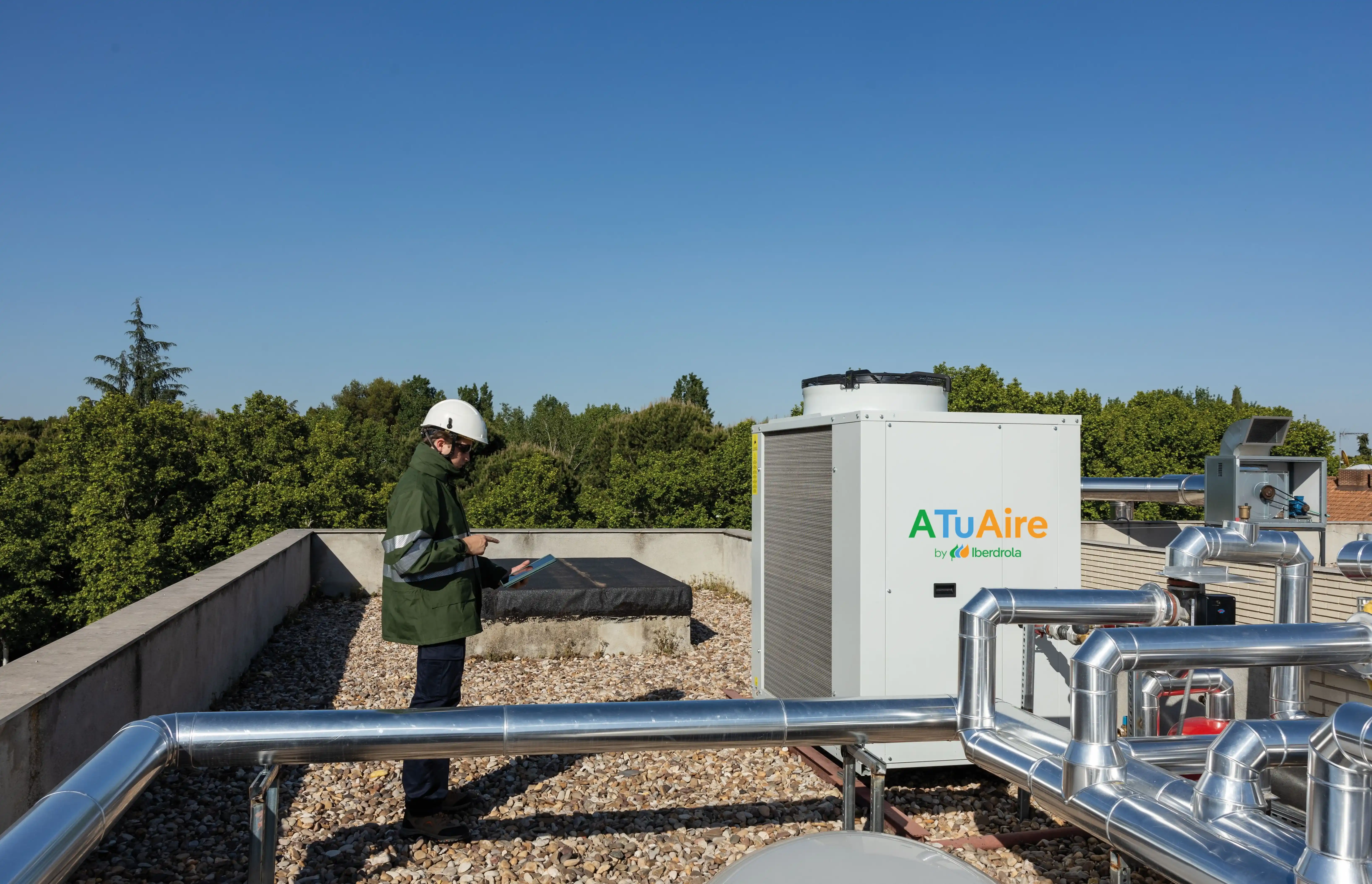 Técnico inspecciona un sistema de aerotermia en la cubierta de un edificio con equipos de climatización y tuberías.