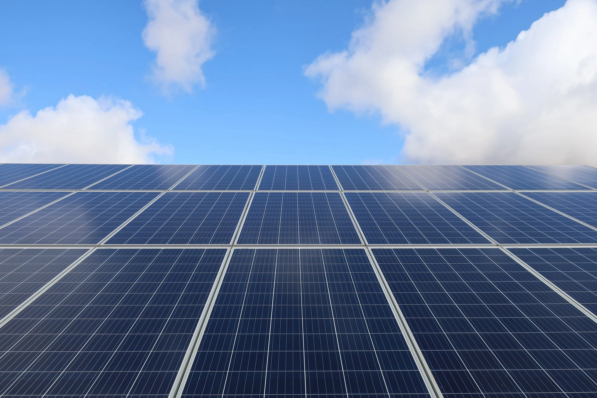 Rows of photovoltaic solar panels under a blue sky with clouds.