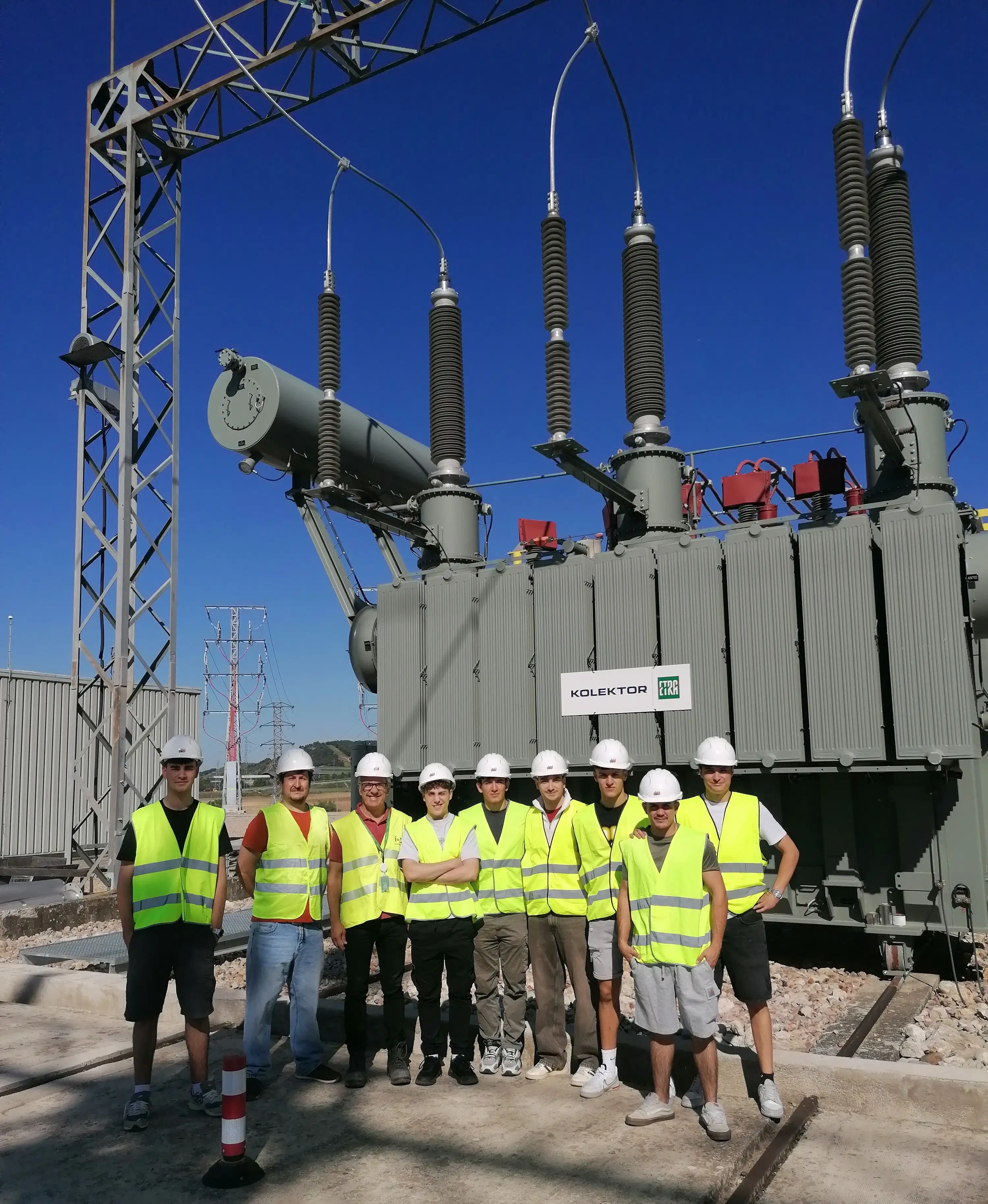 Students wearing safety vests next to an electrical transformer at a substation.