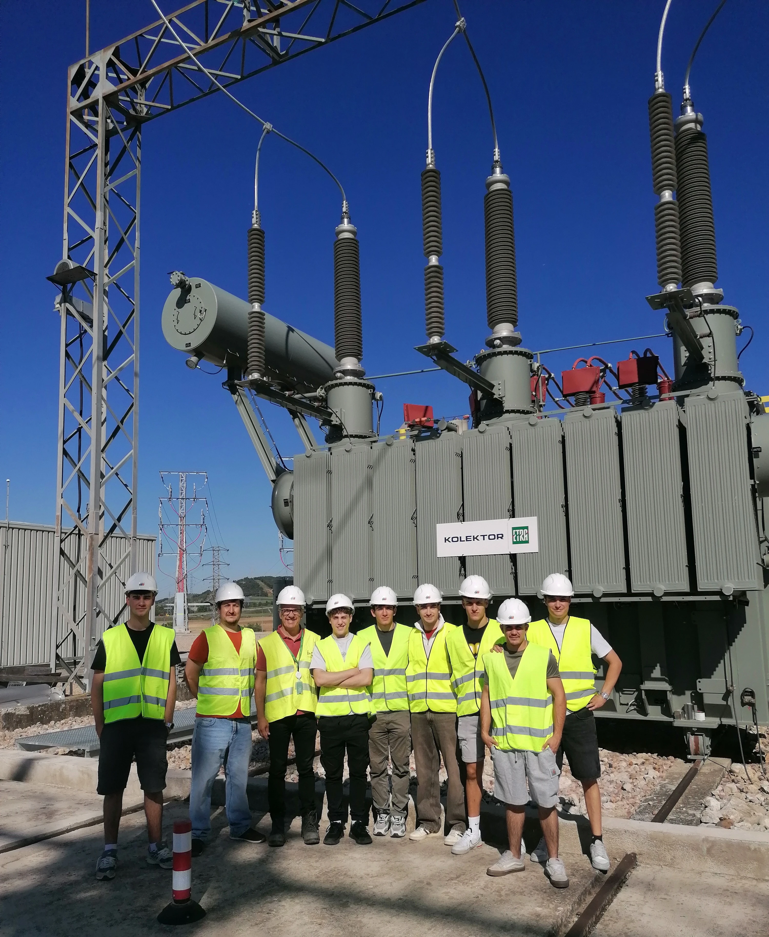 Estudiantes con chalecos de seguridad junto a un transformador eléctrico en una subestación.