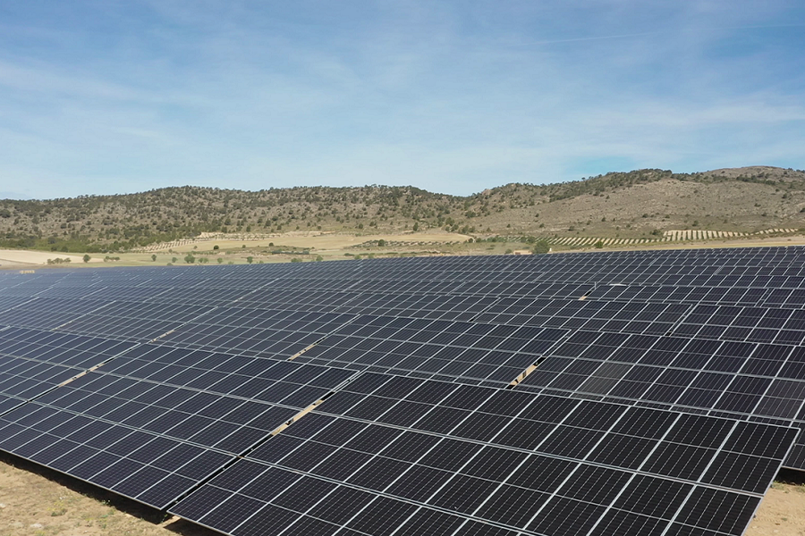 Campo de paneles solares dispuestos en filas, con colinas al fondo y un cielo despejado.