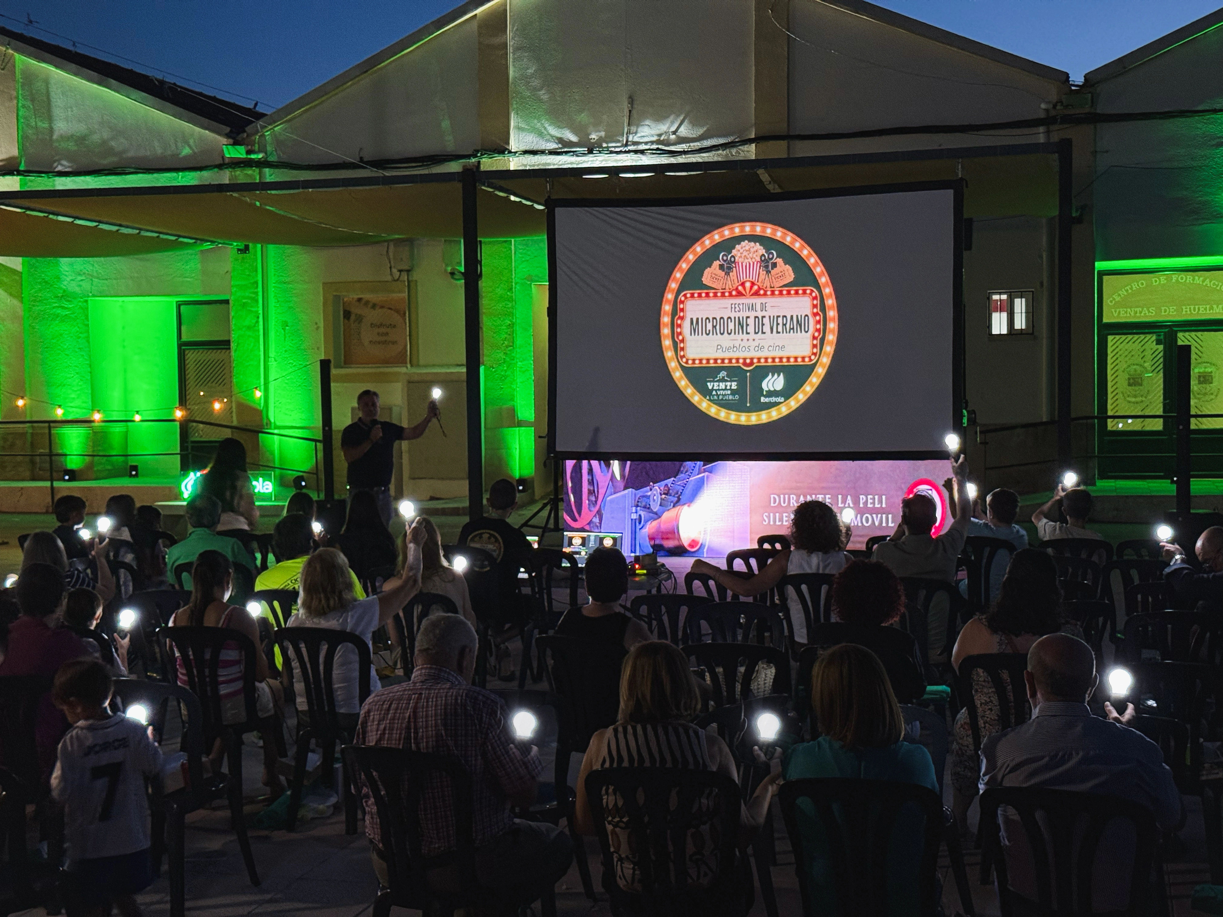 Asistentes participan en una sesión del Festival de Microcine de Verano al aire libre, iluminando el recinto con linternas.