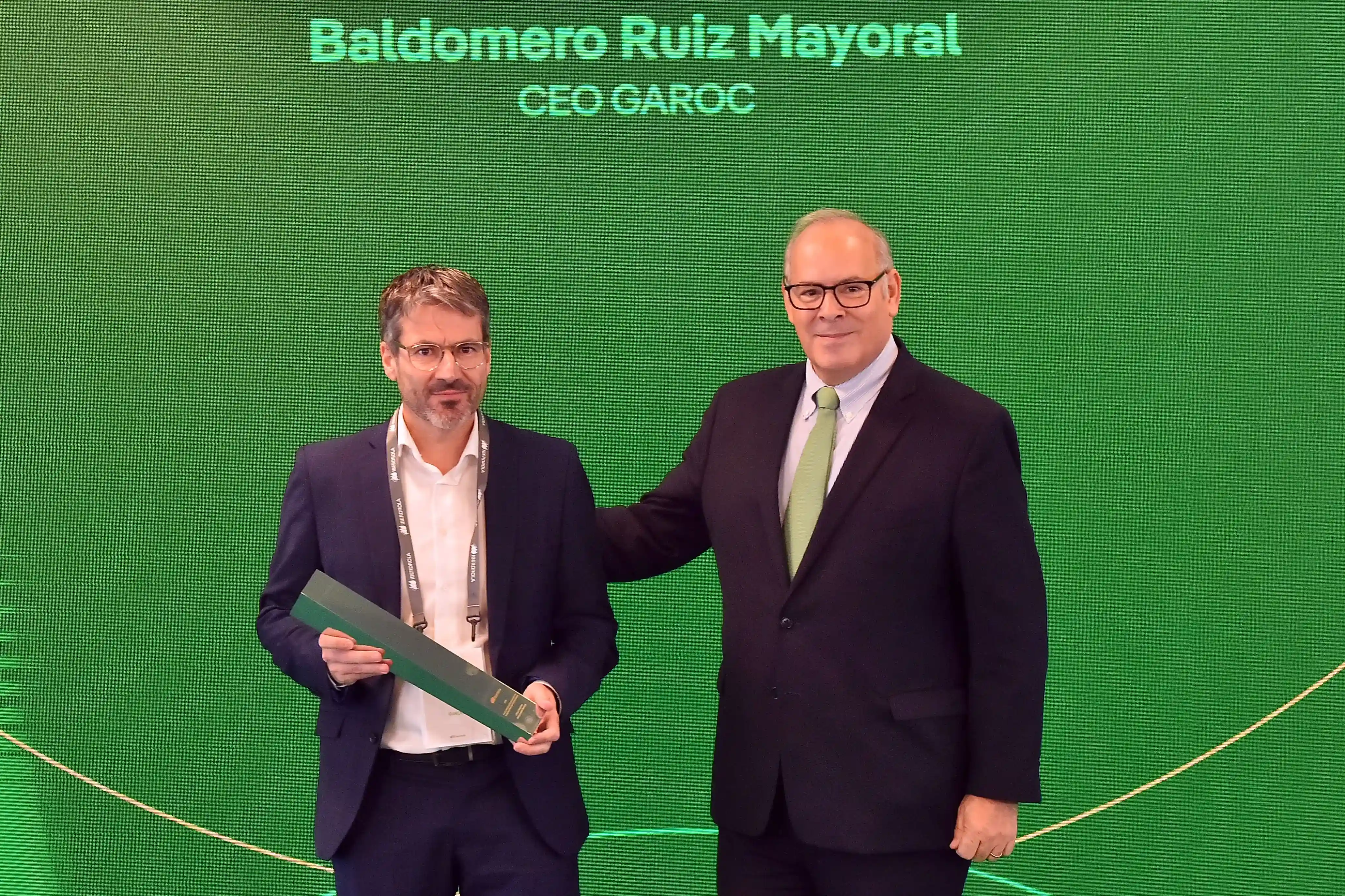 Mario Ruiz-Tagle entrega un premio a Baldomero Ruiz Mayoral, CEO de GAROC, durante un acto corporativo con fondo verde institucional.