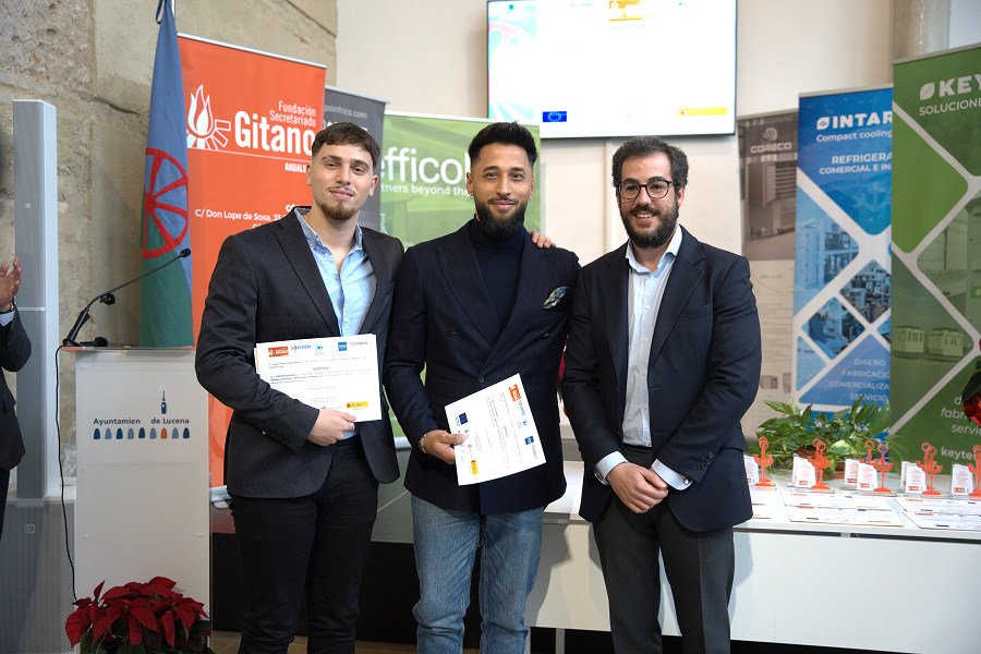 Tres hombres de pie, sonriendo, sosteniendo certificados en una ceremonia de premios