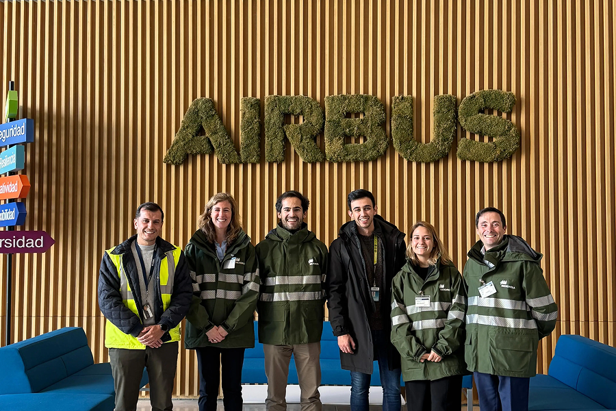 Seis personas posando frente a una pared con el logo de Airbus, compuesto de letras verdes hechas de musgo. Cuatro de ellos están vestidos con chaquetas verdes y reflectantes de Iberdrola. A la izquierda, una persona lleva chaleco de seguridad amarillo.