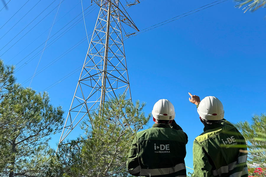 Imagen de dos trabajadores con casco de seguridad observando una torre de energía eléctrica, mientras uno de ellos señala hacia ella.