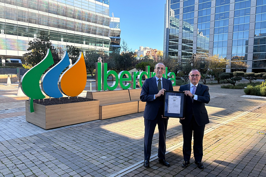 Photo of two people holding a certificate in front of the Iberdrola logo outside a building.
