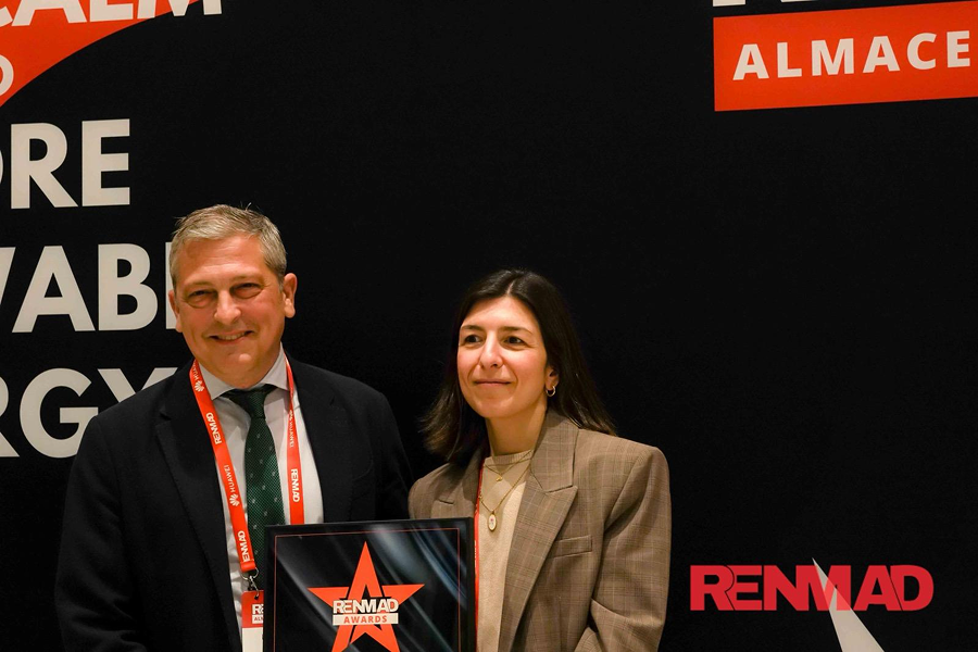 Dos profesionales posan con un premio en un evento del sector energético con logotipo de RENMAD al fondo.