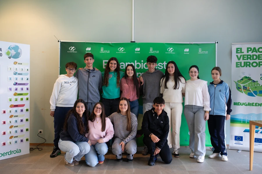 Un grupo de 12 estudiantes posando frente a una pancarta verde con el texto "Cambiemos el Futuro". Están de pie y sentados, son 7 chicos y 5 chicas, vestidos con ropa casual. A la izquierda se ve una cartelería con iconos de energías renovables, mientras que a la derecha hay una cartelera con el texto "El Pacto Verde Europeo".
