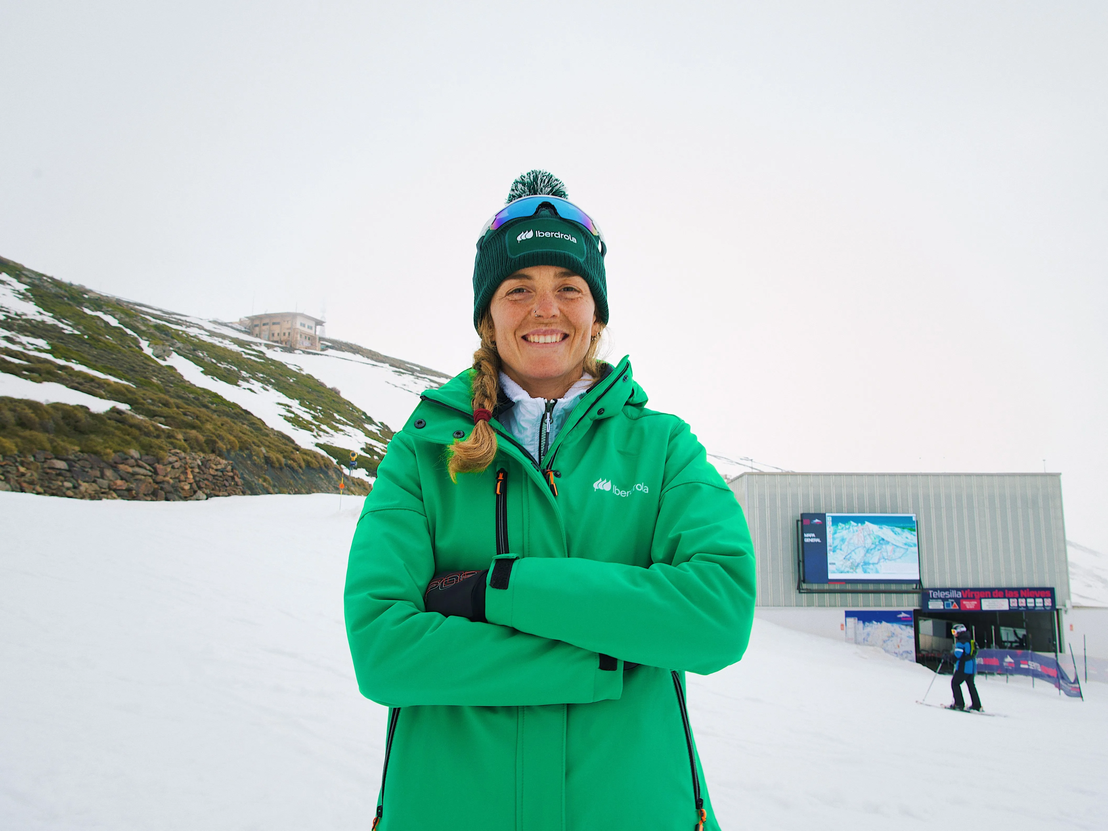 Esquiadora Ana Alonso, embajadora de Iberdrola, posa en la estación de esquí con abrigo verde y gorro de la empresa.