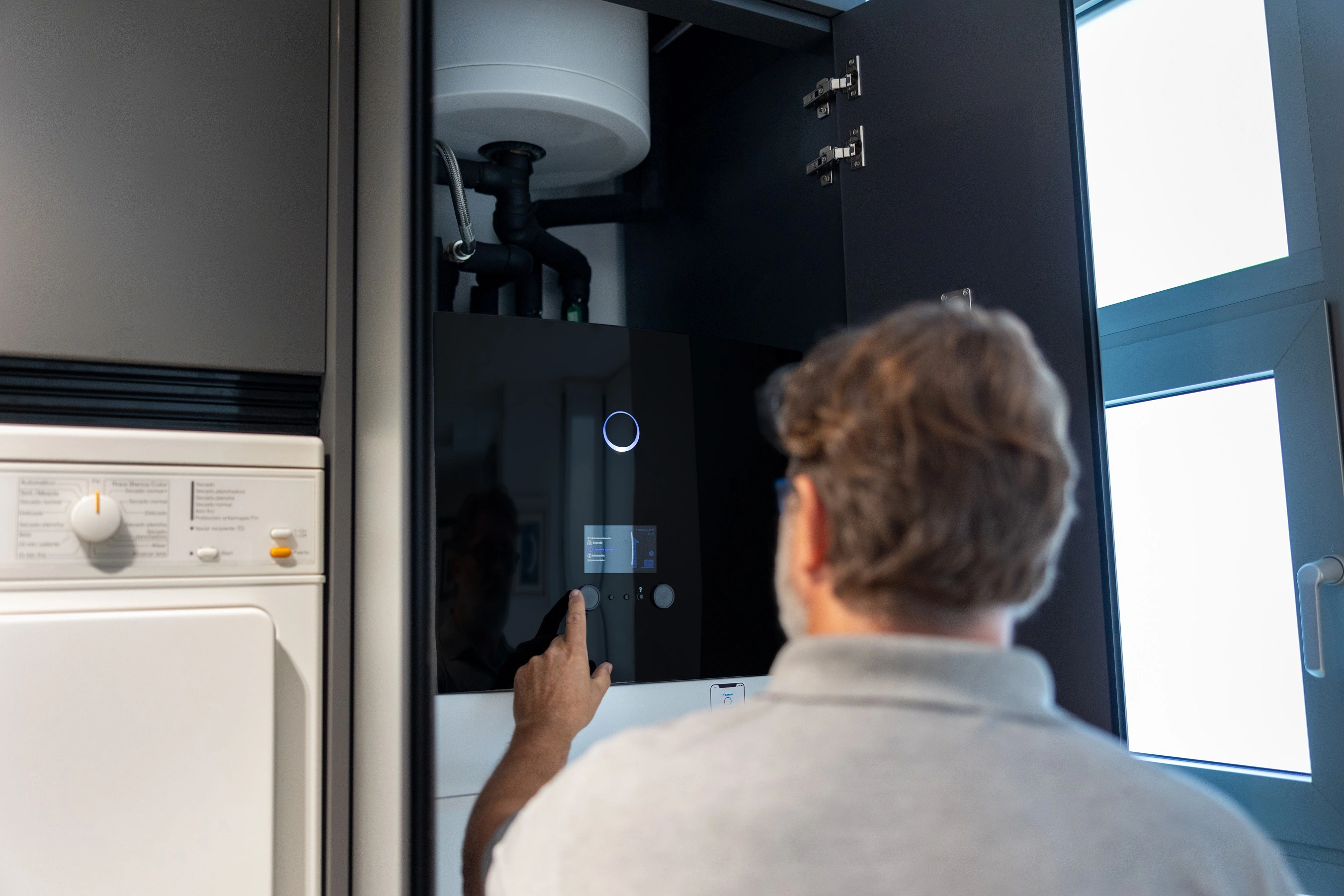 Persona interactuando con una unidad de aerotermia en una vivienda, tocando la pantalla de control del sistema