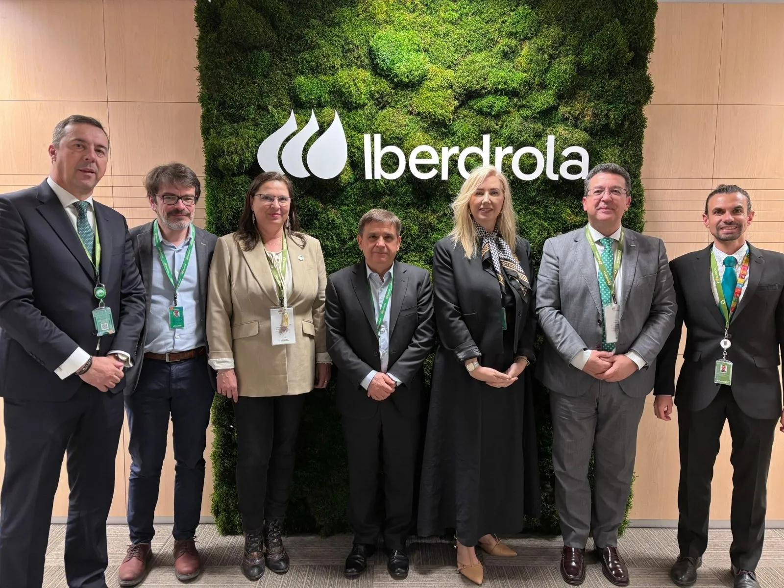Equipo directivo posa ante logo de Iberdrola sobre pared vegetal en sede corporativa