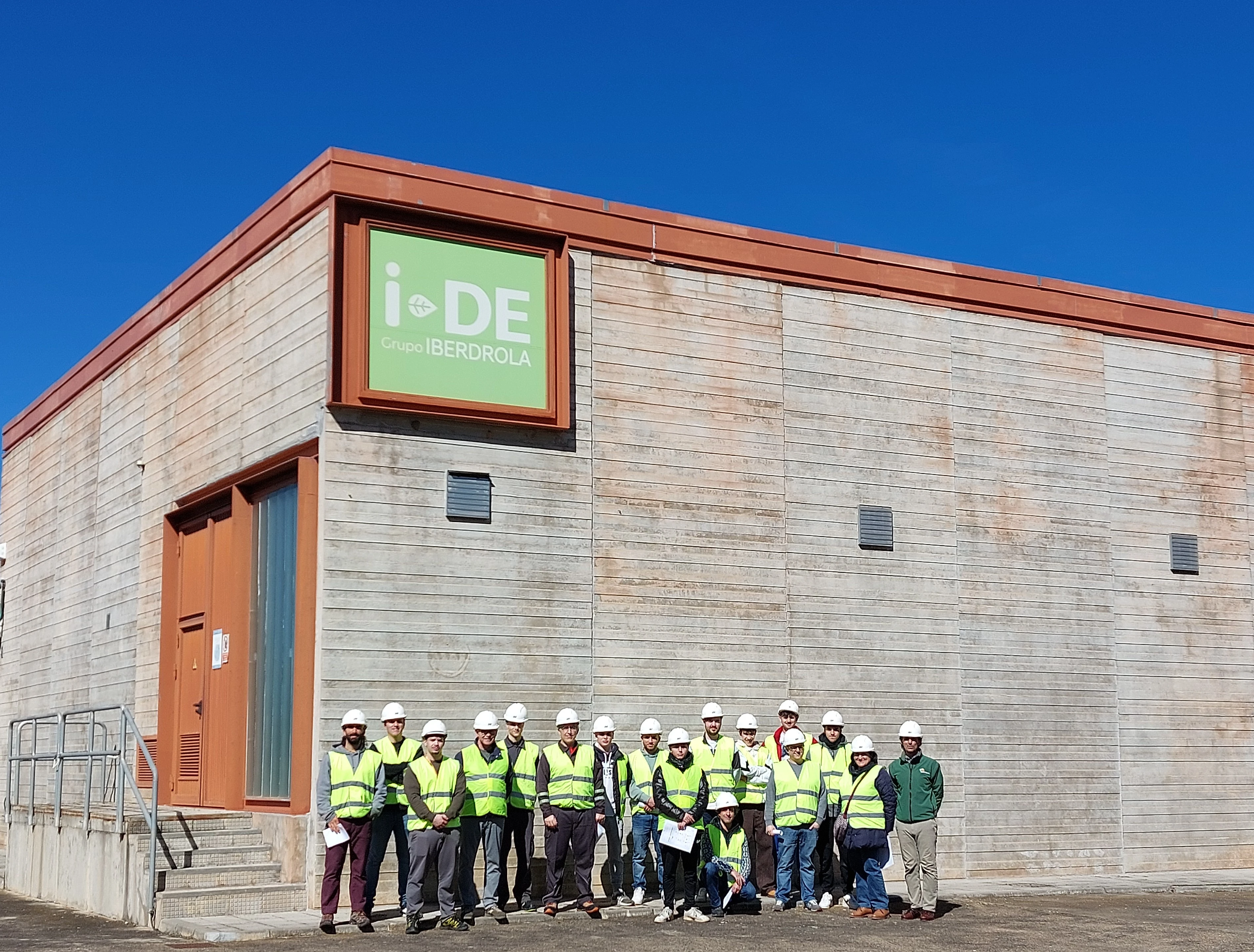 Group of people wearing safety vests and helmets in front of an Iberdrola España building on a sunny day.