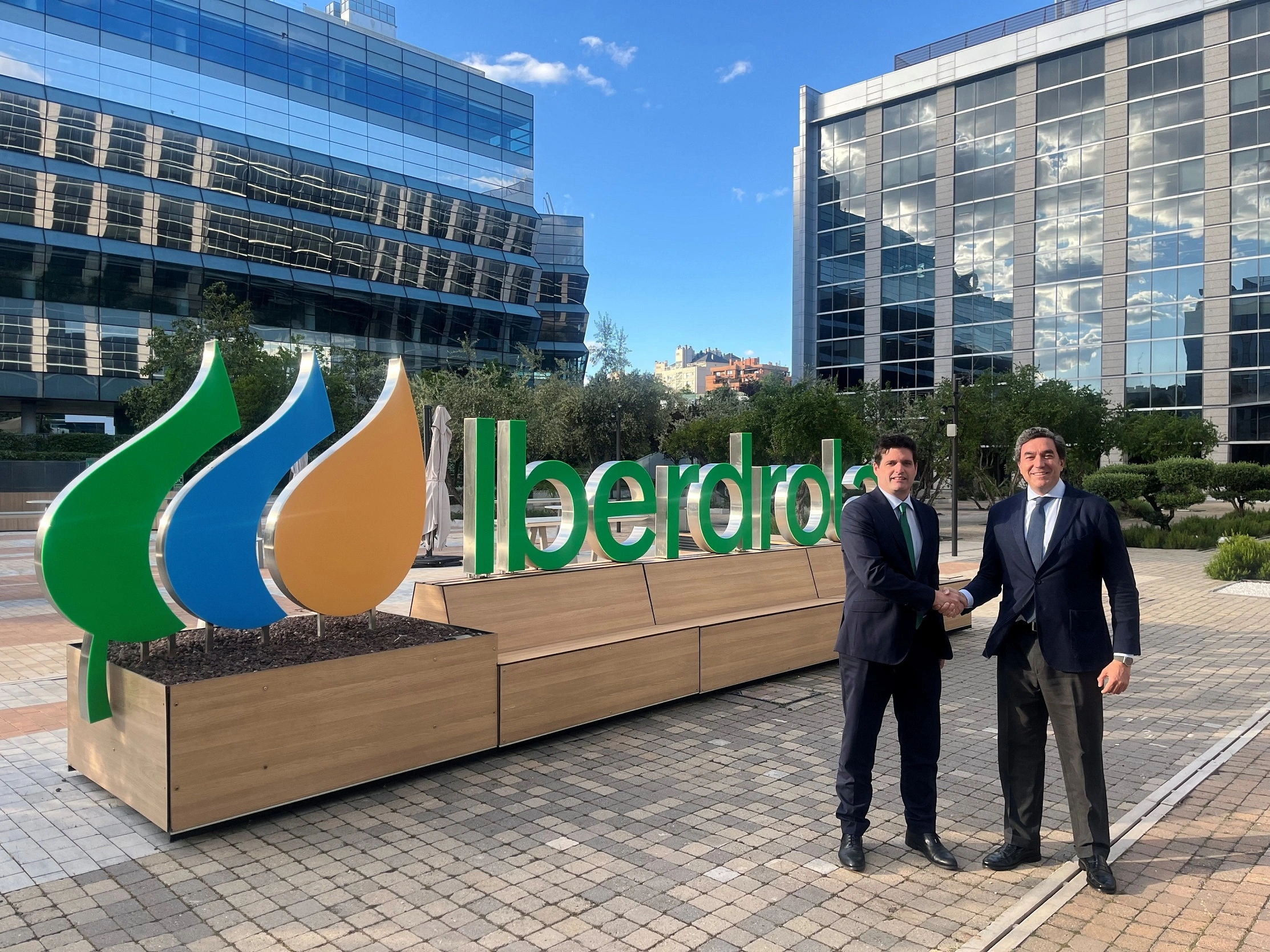 Representantes de Iberdrola y Legalitas estrechan manos frente al logotipo de Iberdrola en el exterior de sus oficinas.