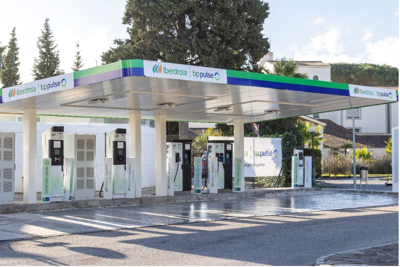 Estación de carga de vehículos eléctricos con los logotipos de Iberdrola y BP Pulse. Se ven varios cargadores en una plataforma techada.