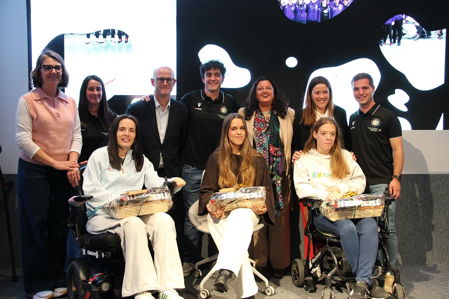 Grupo de personas posando en un foro, incluidas tres mujeres en sillas de ruedas sosteniendo cestas de regalo.