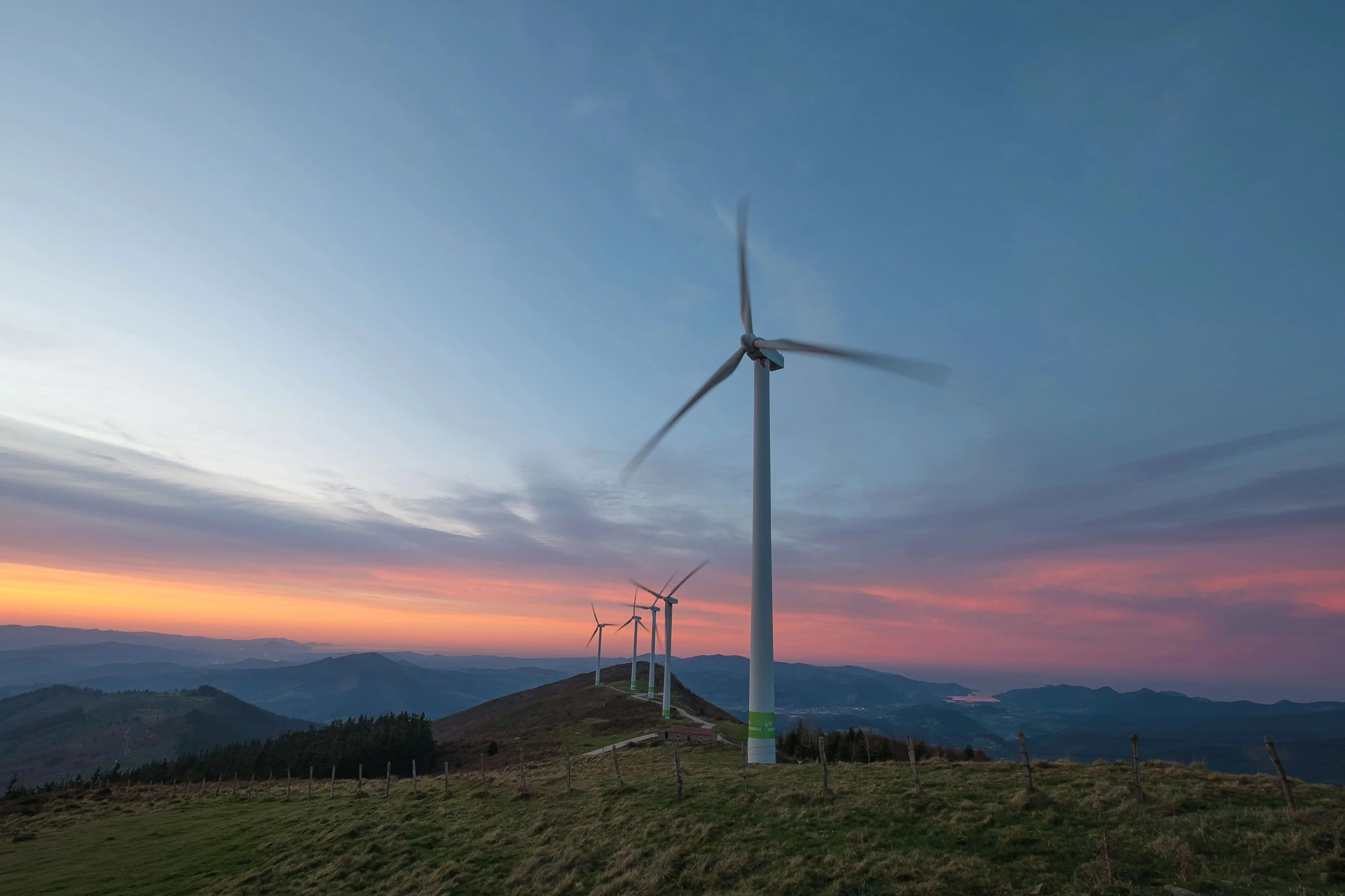 Iberdrola wind turbines on a mountain at sunset, with the landscape lit by blue and pink tones.