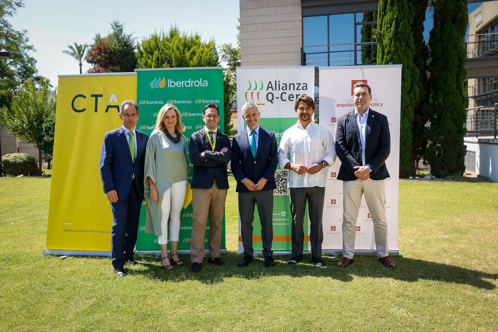 Grupo de seis personas de pie sobre césped frente a carteles de Iberdrola, Alianza Q-Cero y colegio de arquitectura técnica, posando para fotografía al aire libre.