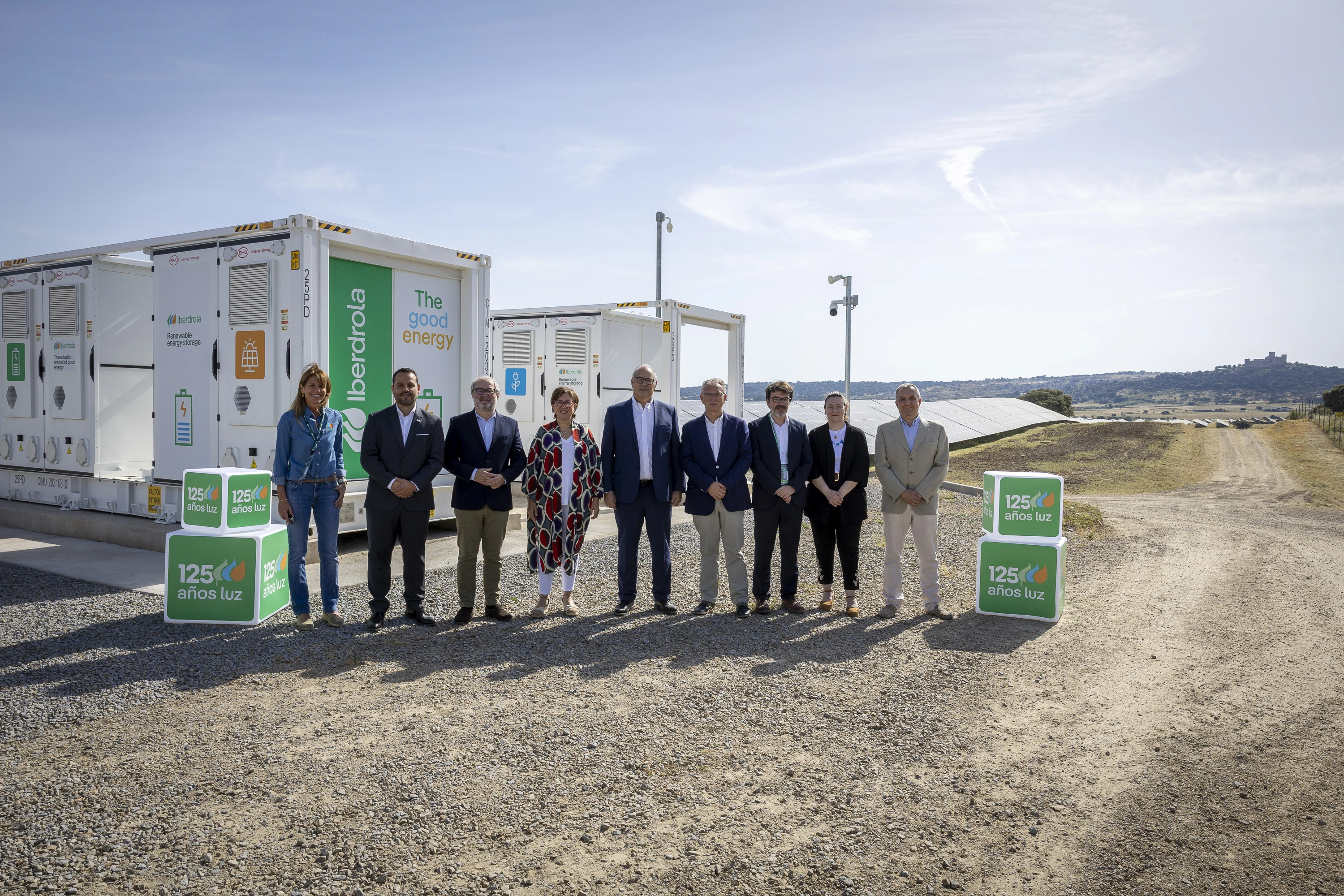 Group of people standing in front of Iberdrola renewable energy storage containers, with solar panels and open landscape in the background.