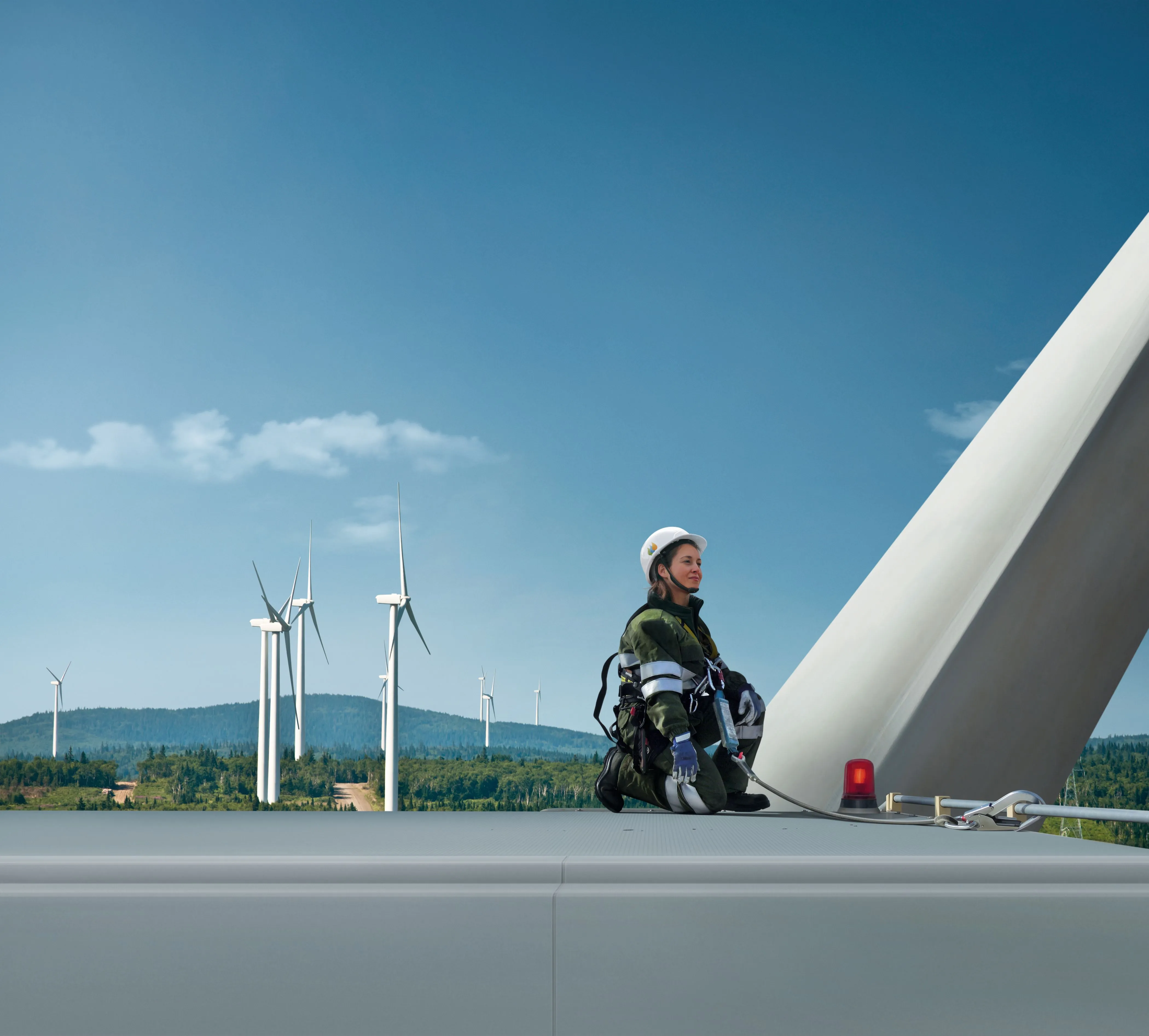 Técnica de mantenimiento de Iberdrola trabajando sobre un aerogenerador, con arneses de seguridad y varios molinos de viento visibles al fondo.