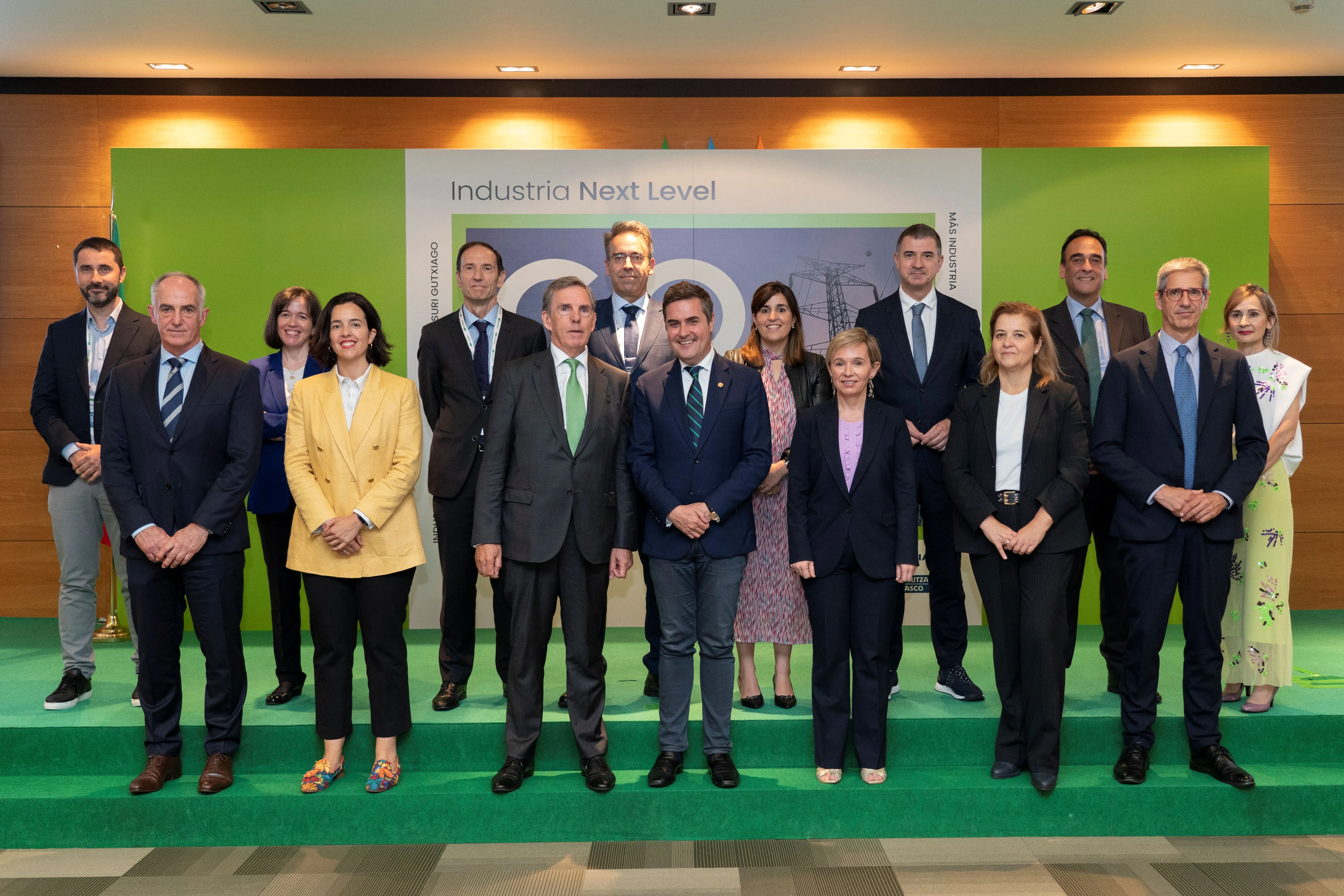 Group of fifteen people posing in front of a panel reading “Industria Next Level” at a corporate event, dressed in formal attire.