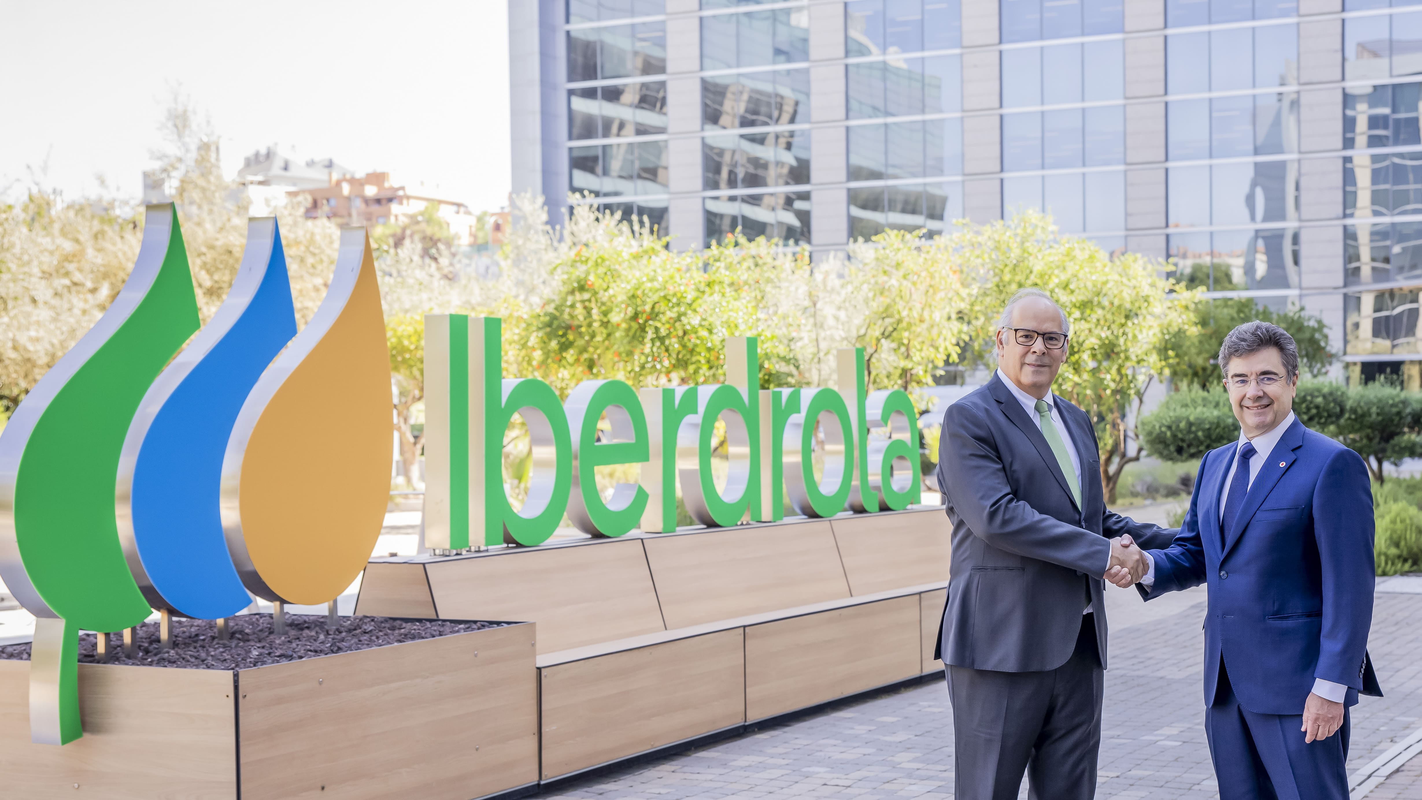 Mario Ruiz-Tagle, CEO of Iberdrola España, and José Miguel García, CEO of Vodafone España, shaking hands in front of an Iberdrola logo outdoors, with office buildings in the background.