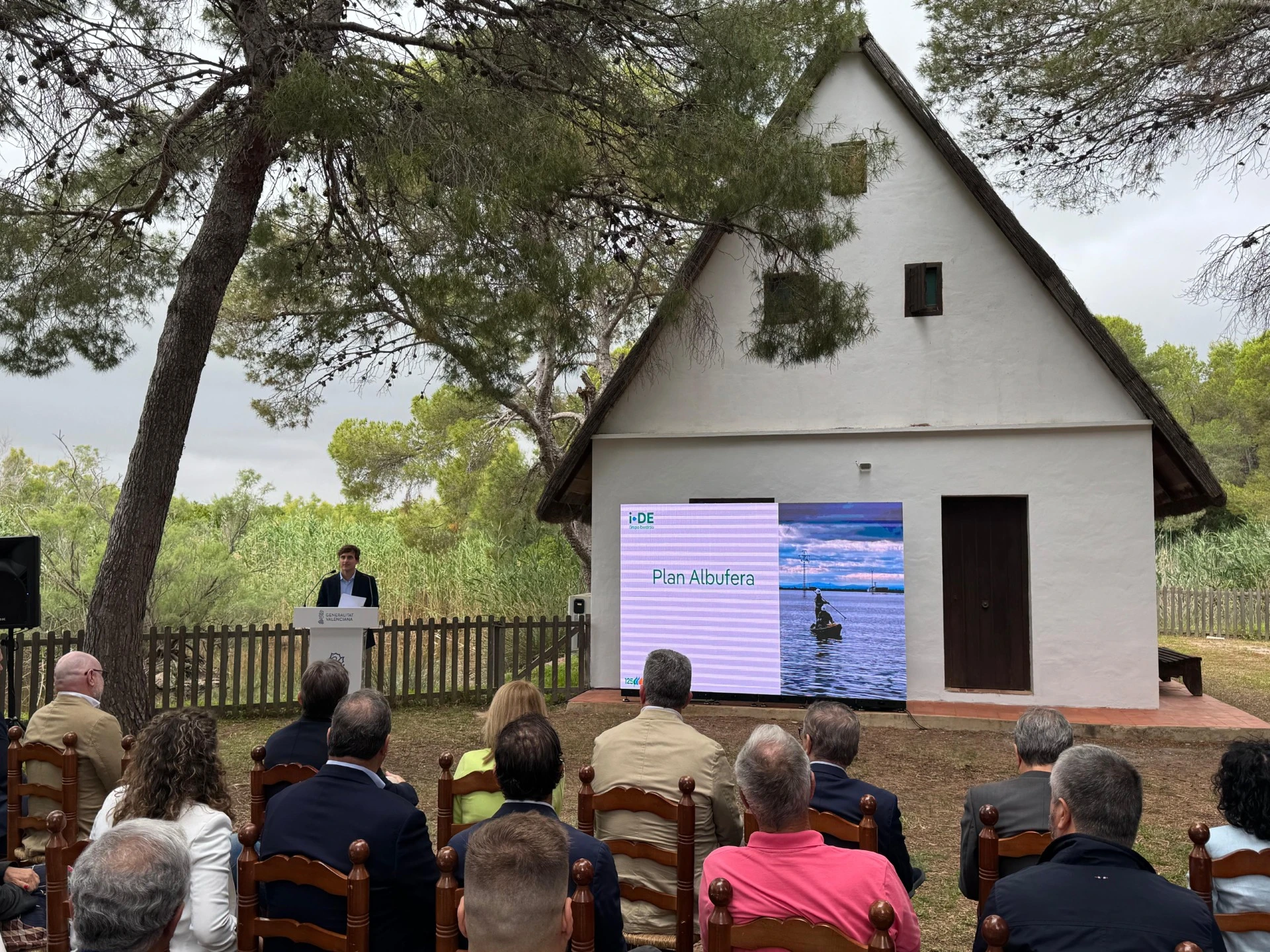 Presentación del Plan Albufera de la Generalitat Valenciana al aire libre, con público sentado en sillas de madera, un ponente en el atril y pantalla con información del plan junto a una caseta blanca.