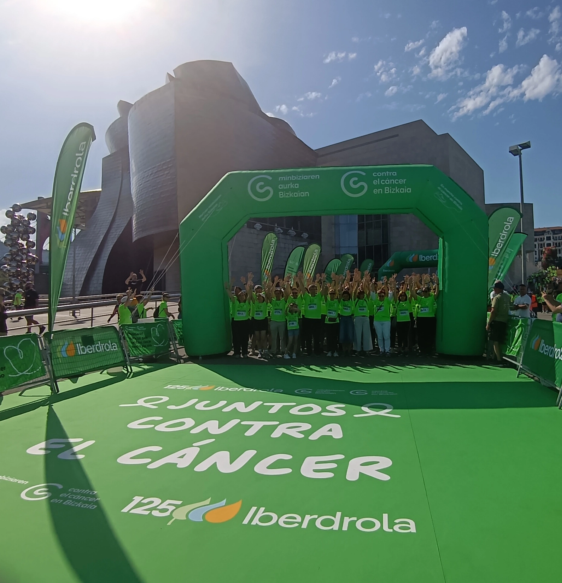 Participantes de una marcha solidaria contra el cáncer posan bajo el arco de salida patrocinado por Iberdrola en Bilbao.