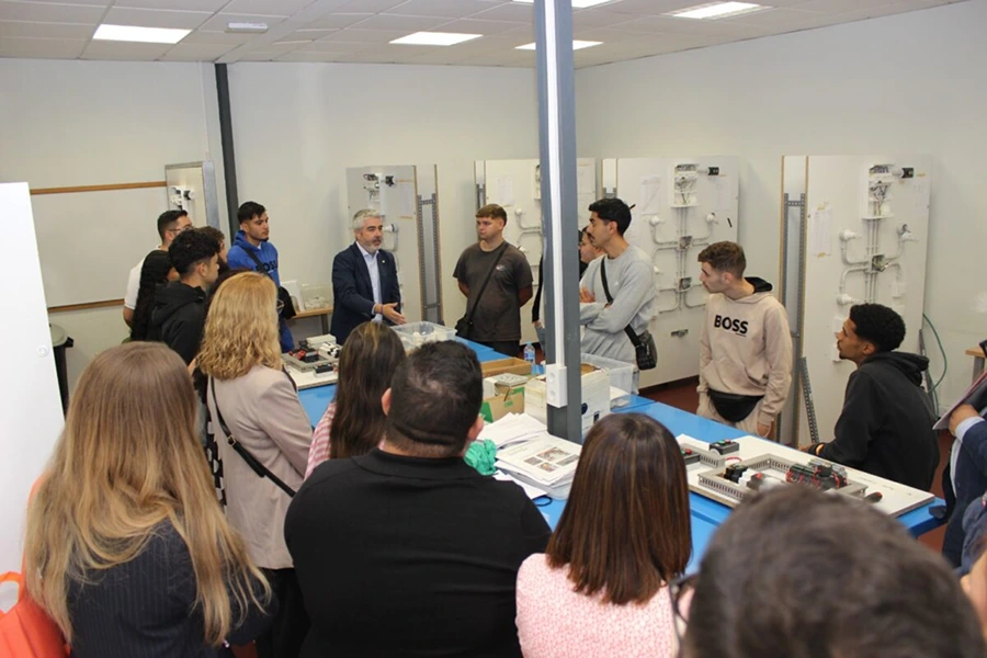 Un grupo de jóvenes participa en una sesión de formación sobre instalaciones eléctricas en un aula técnica, guiados por un instructor.