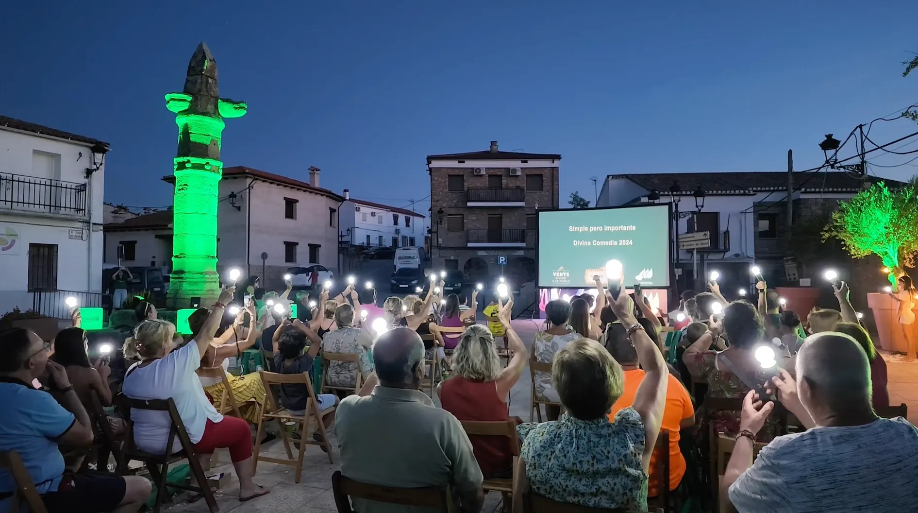 Audience attending an outdoor nighttime screening in an illuminated square