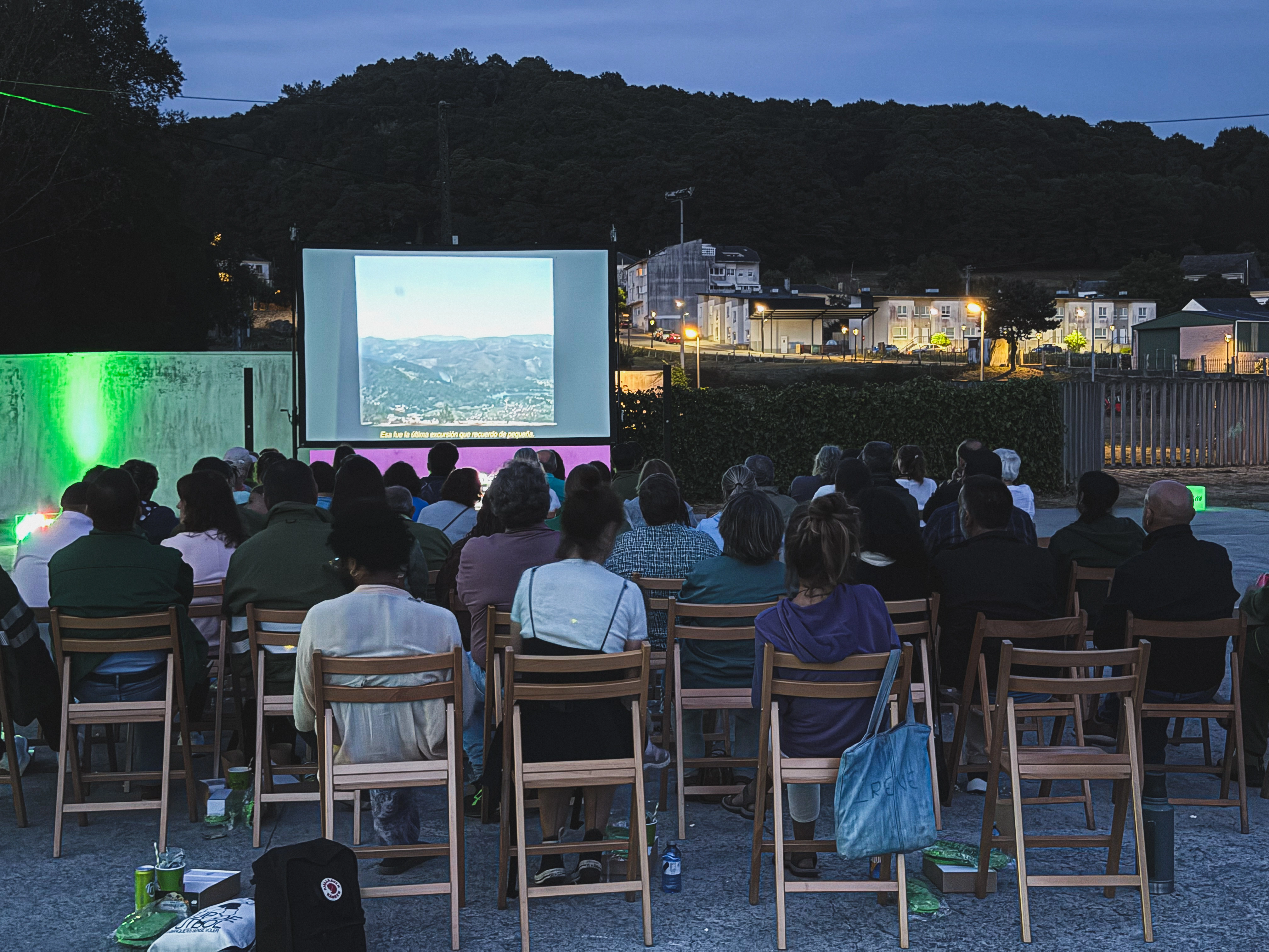 Público asistiendo a una proyección audiovisual al aire libre al anochecer