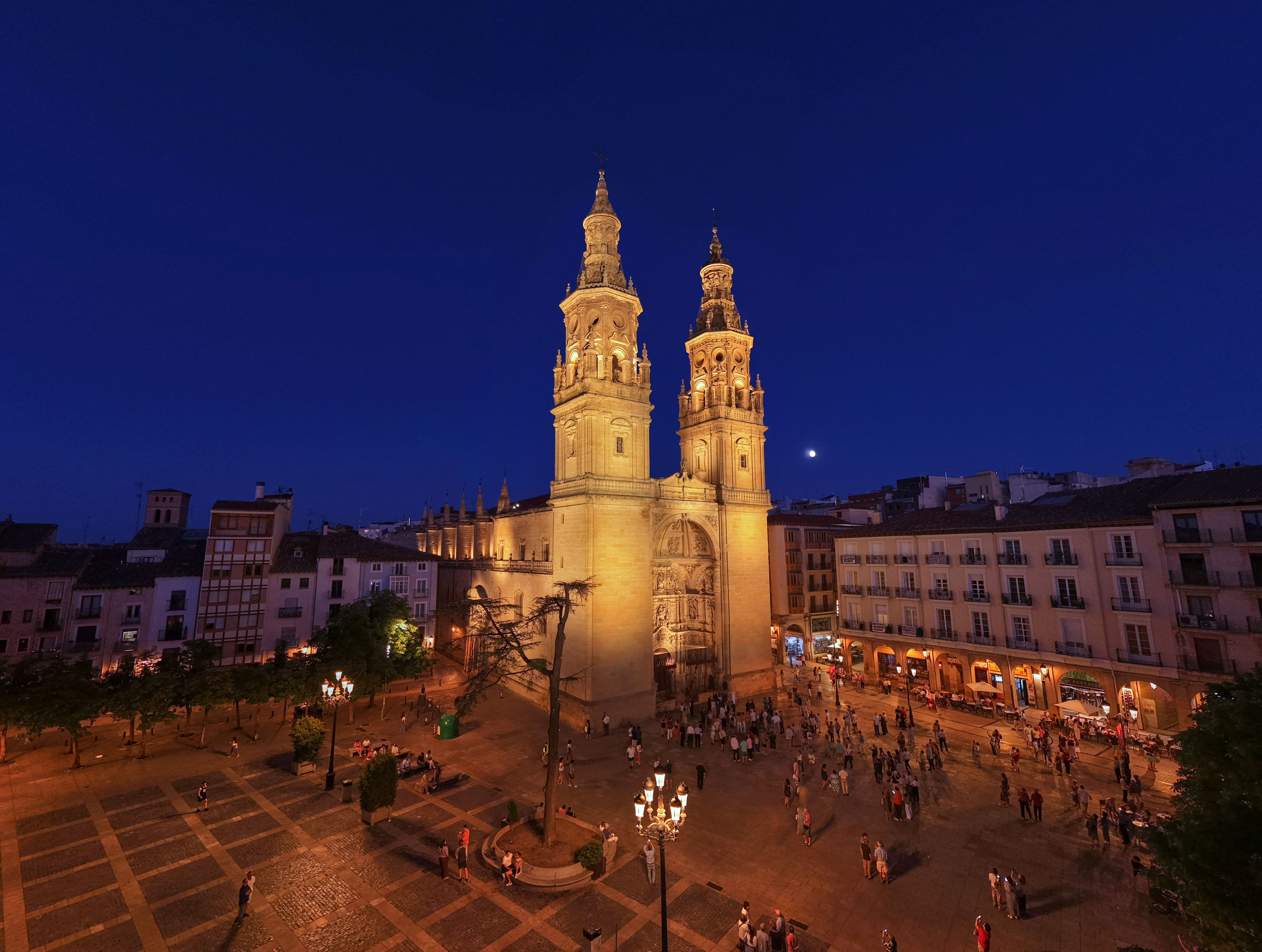 Catedral iluminada al anochecer en una plaza urbana con edificios históricos alrededor.