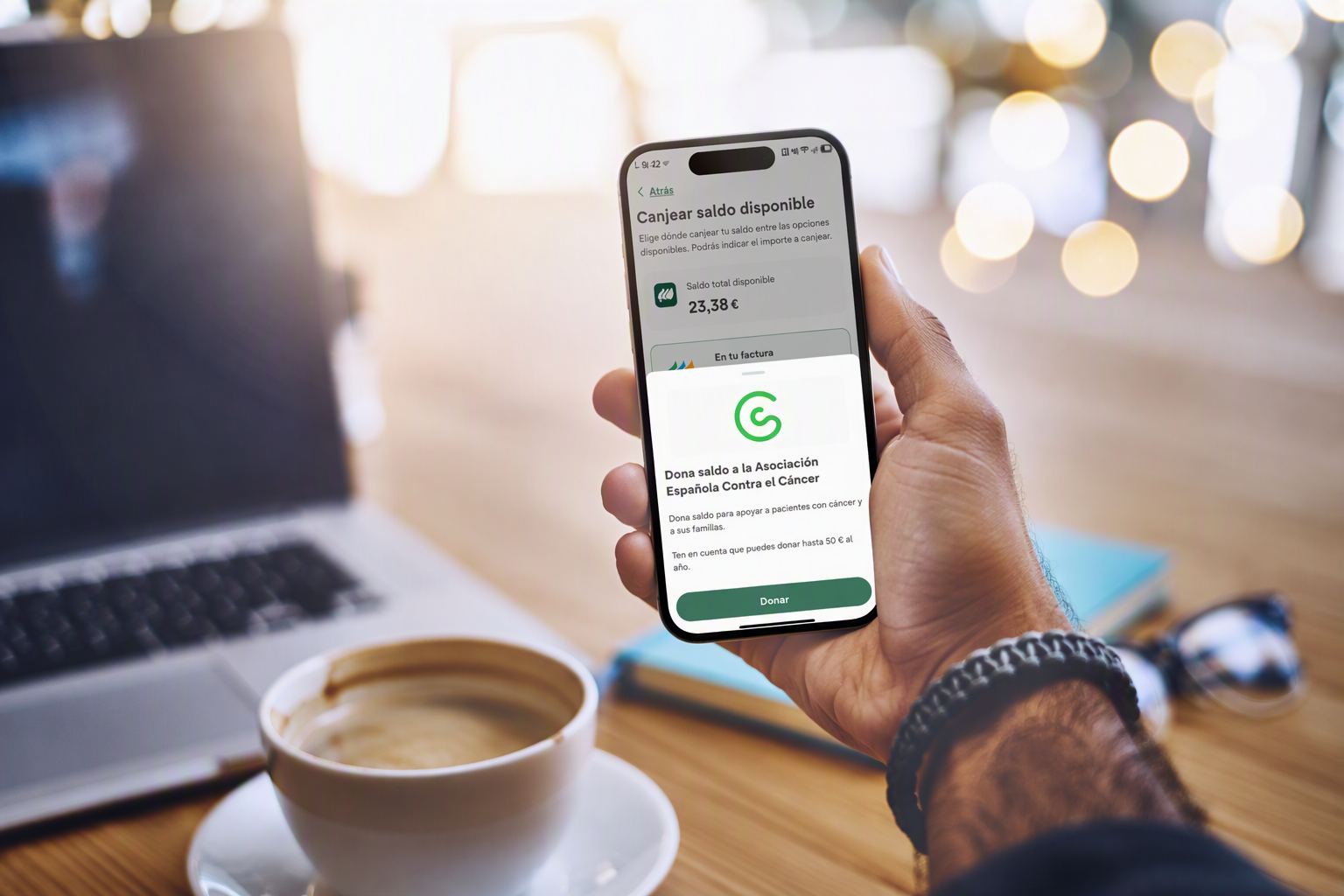 Una persona utiliza la aplicación Mi Iberdrola en su móvil para donar saldo disponible a la Asociación Española Contra el Cáncer. En la pantalla aparece un saldo de 23,38 euros y la opción «Donar».
