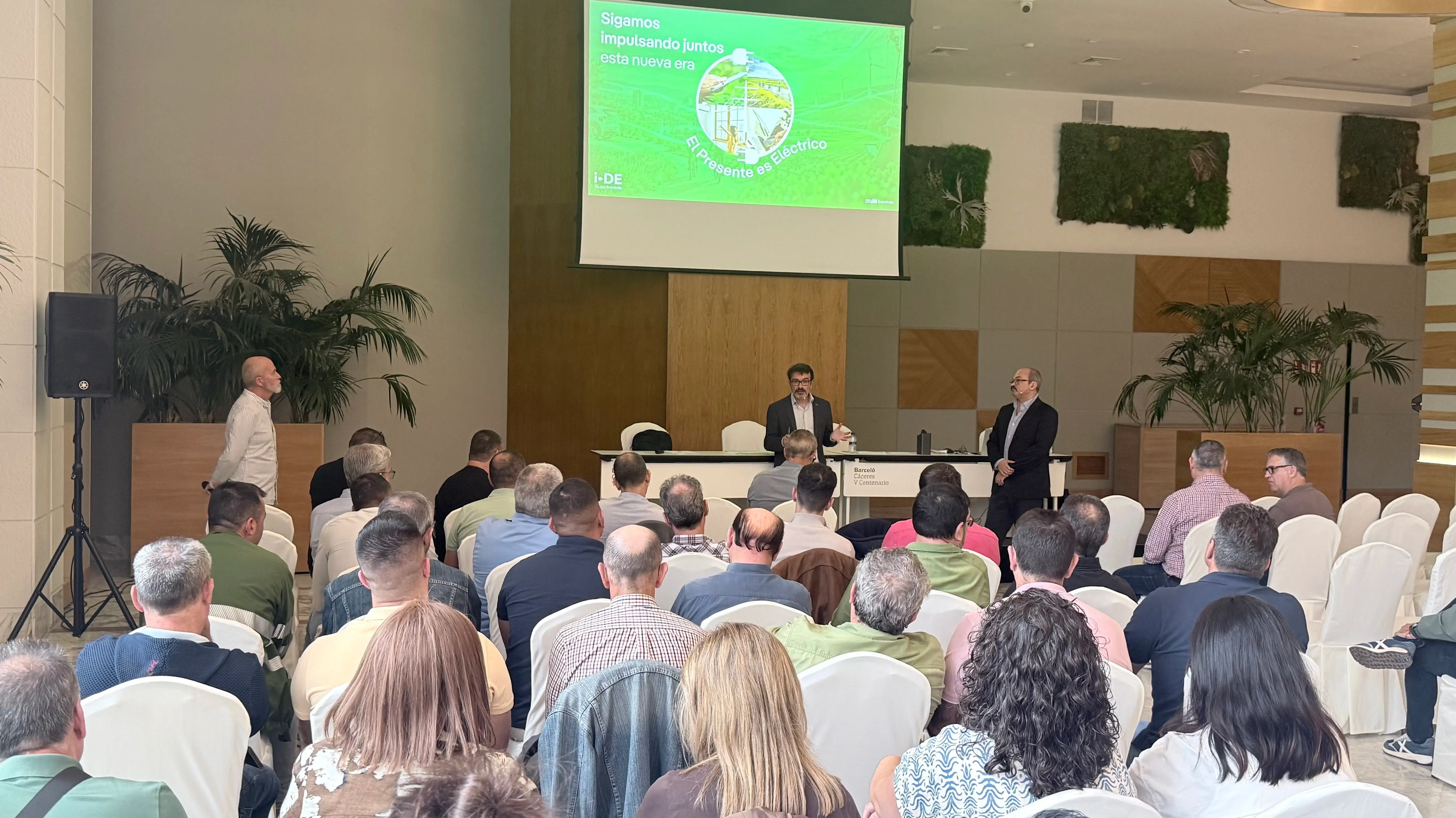Ponentes y asistentes en un encuentro de i-DE en Cáceres, con el lema «El presente es eléctrico» en pantalla.