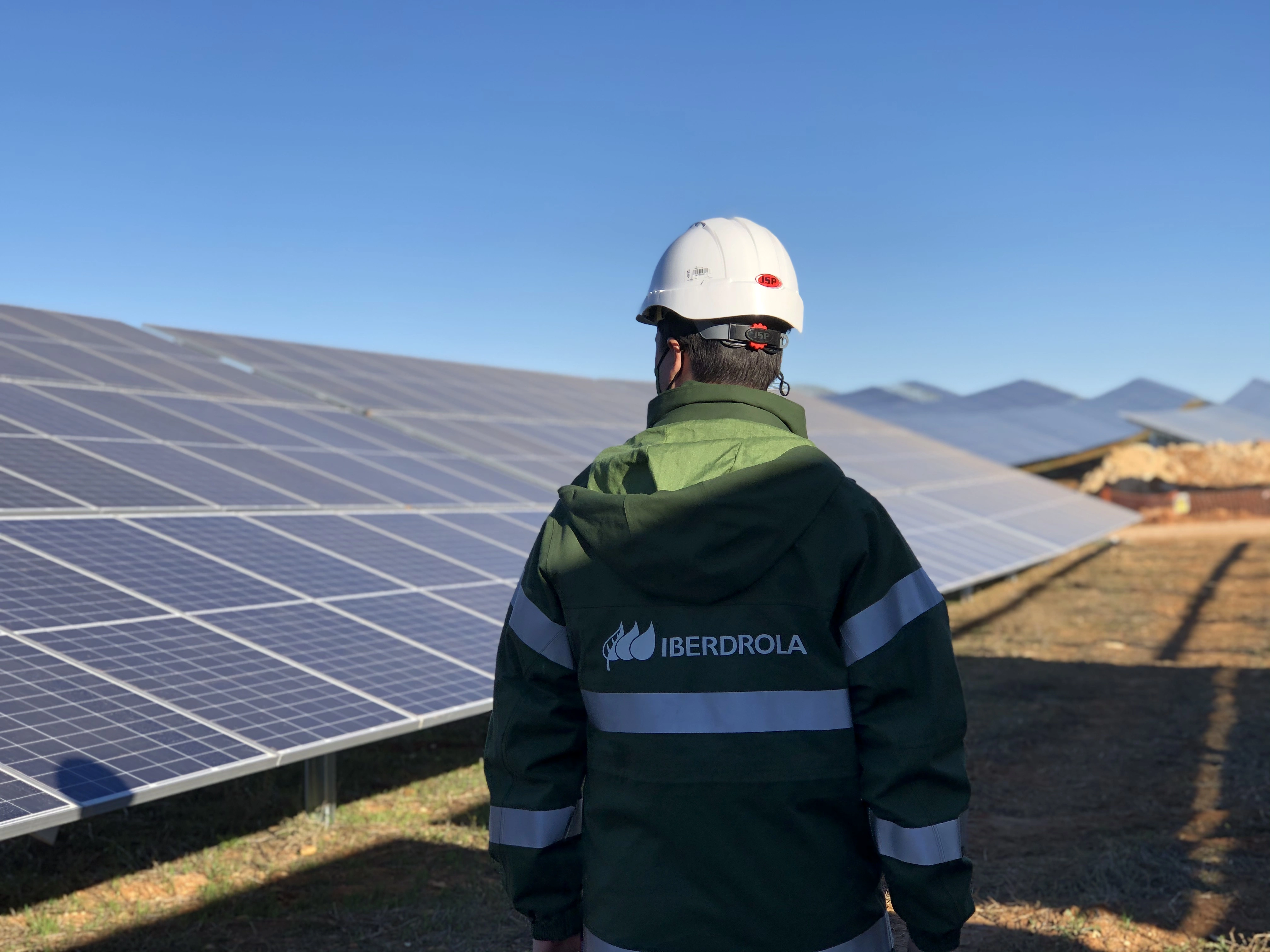 Iberdrola technician wearing a hard hat and green uniform in front of solar panels at a photovoltaic plant.