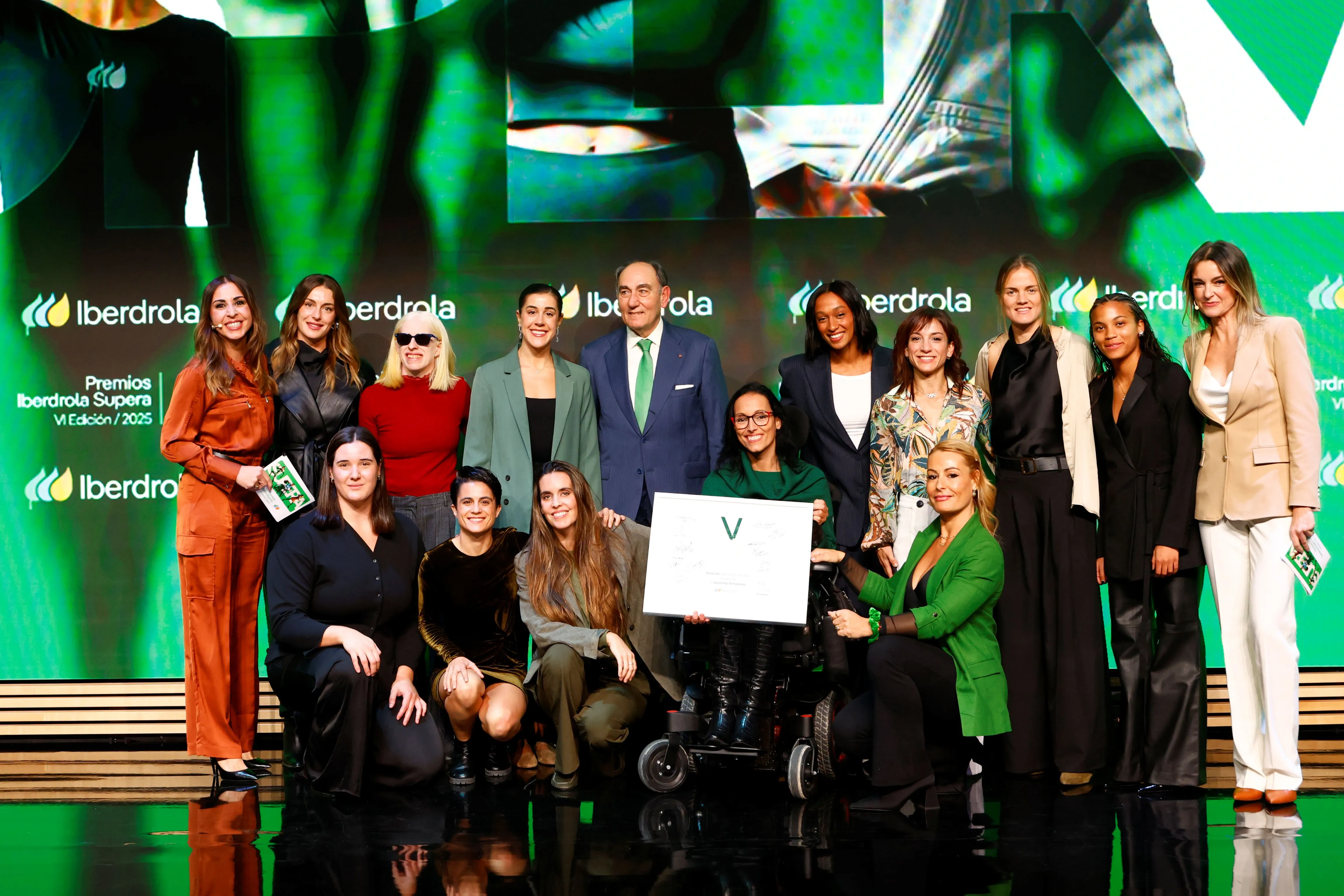 Foto de grupo en ceremonia de Premios Iberdrola Supera con galardonadas y persona en silla de ruedas sosteniendo certificado en escenario.