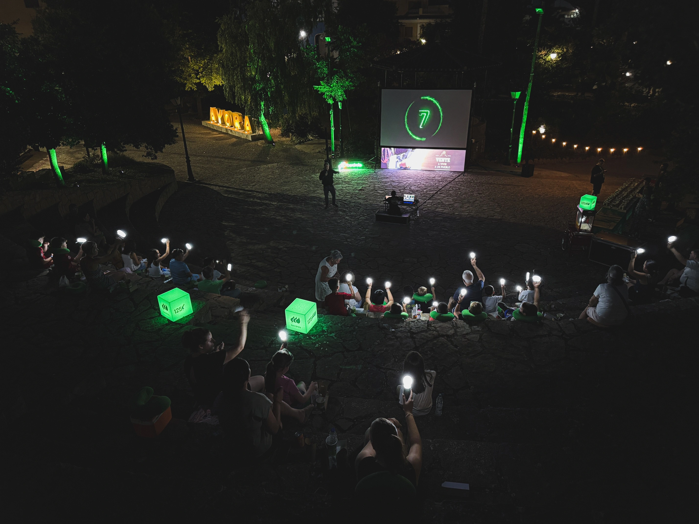 Público asistiendo a una proyección nocturna al aire libre con iluminación verde y elementos de Iberdrola.