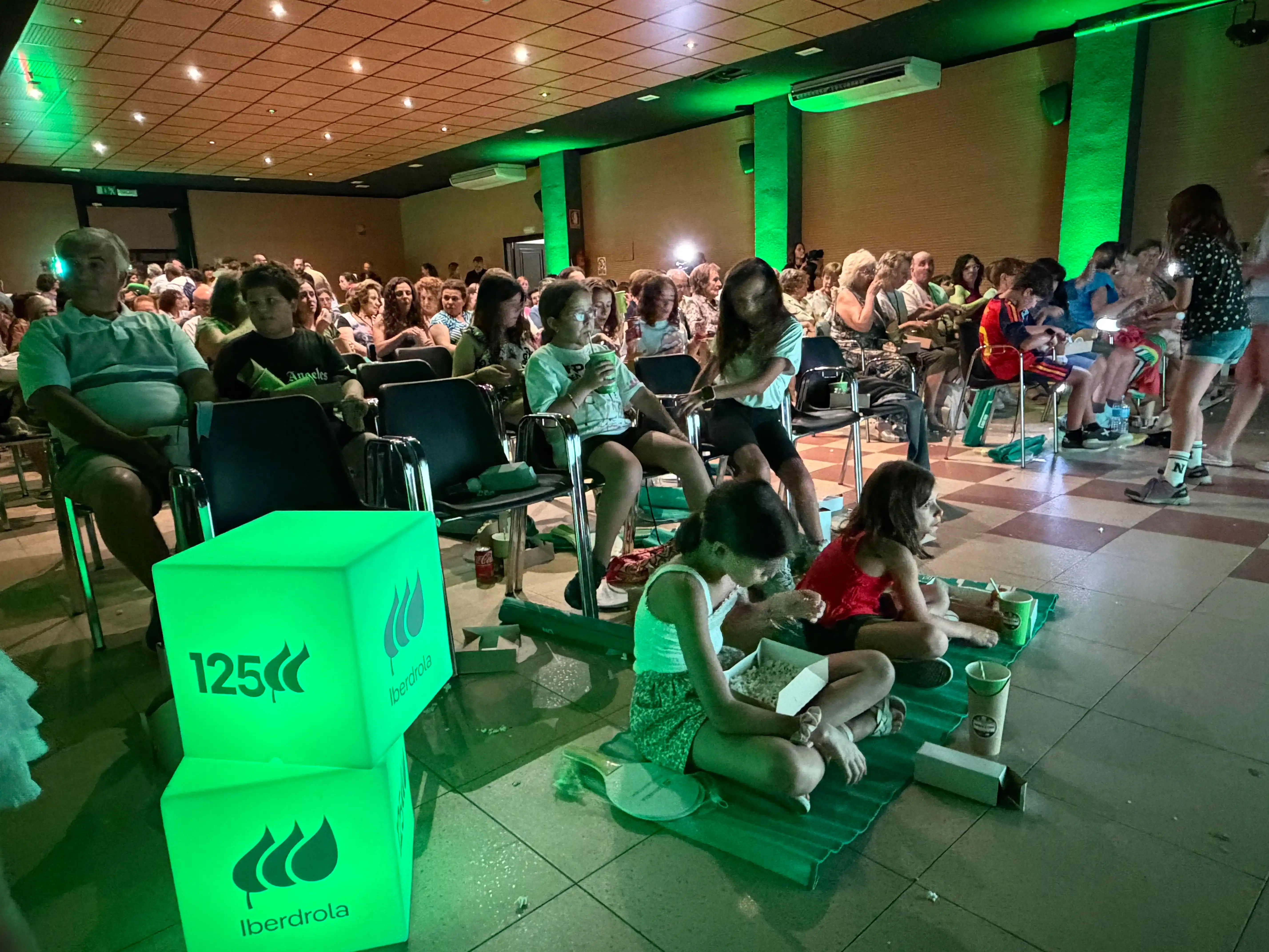 Público de distintas edades reunido en un espacio interior para una sesión del Festival de Microcine de Verano, con asistentes disfrutando de palomitas antes de la proyección.