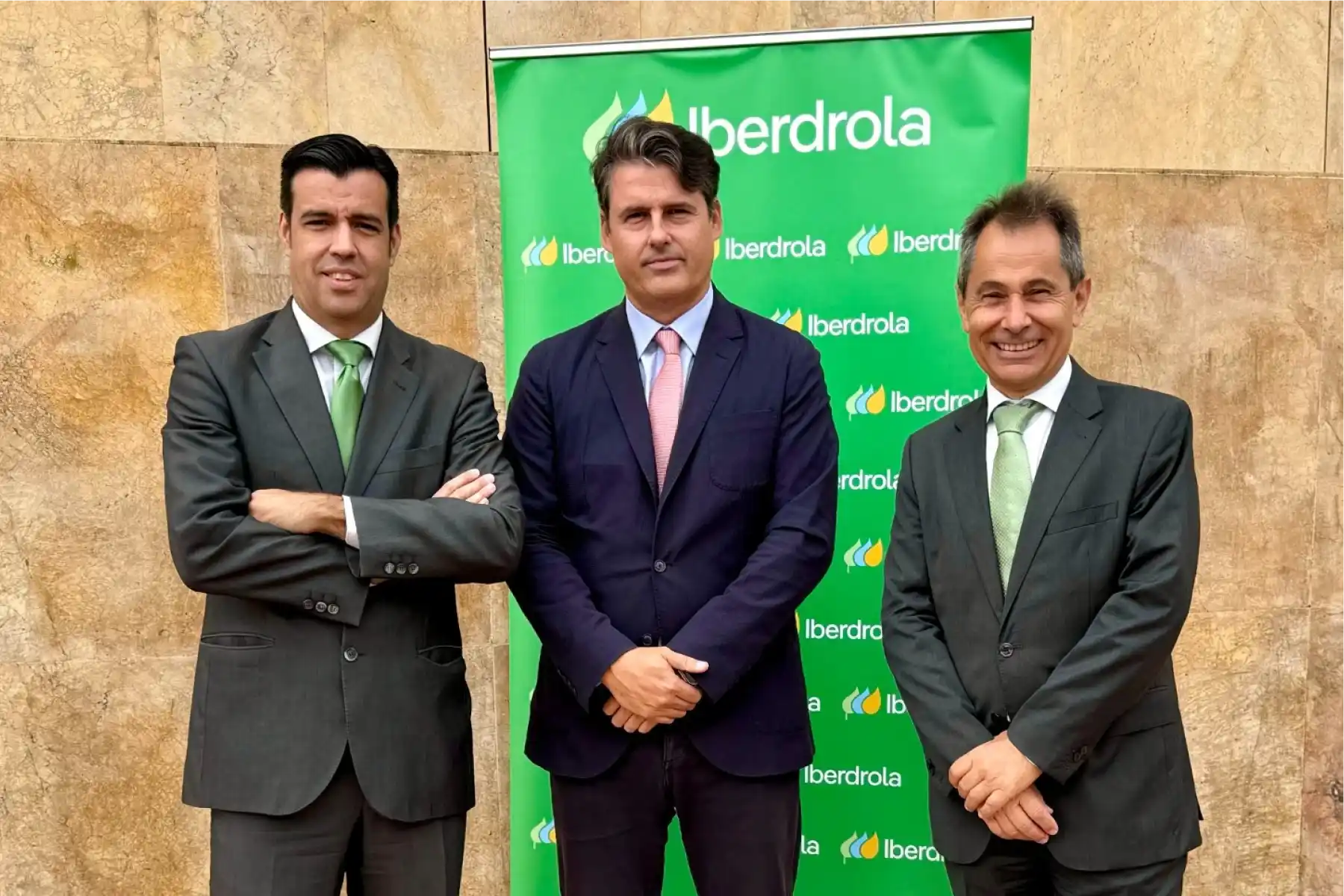 Tres directivos en traje posando frente a fondo corporativo verde de Iberdrola.