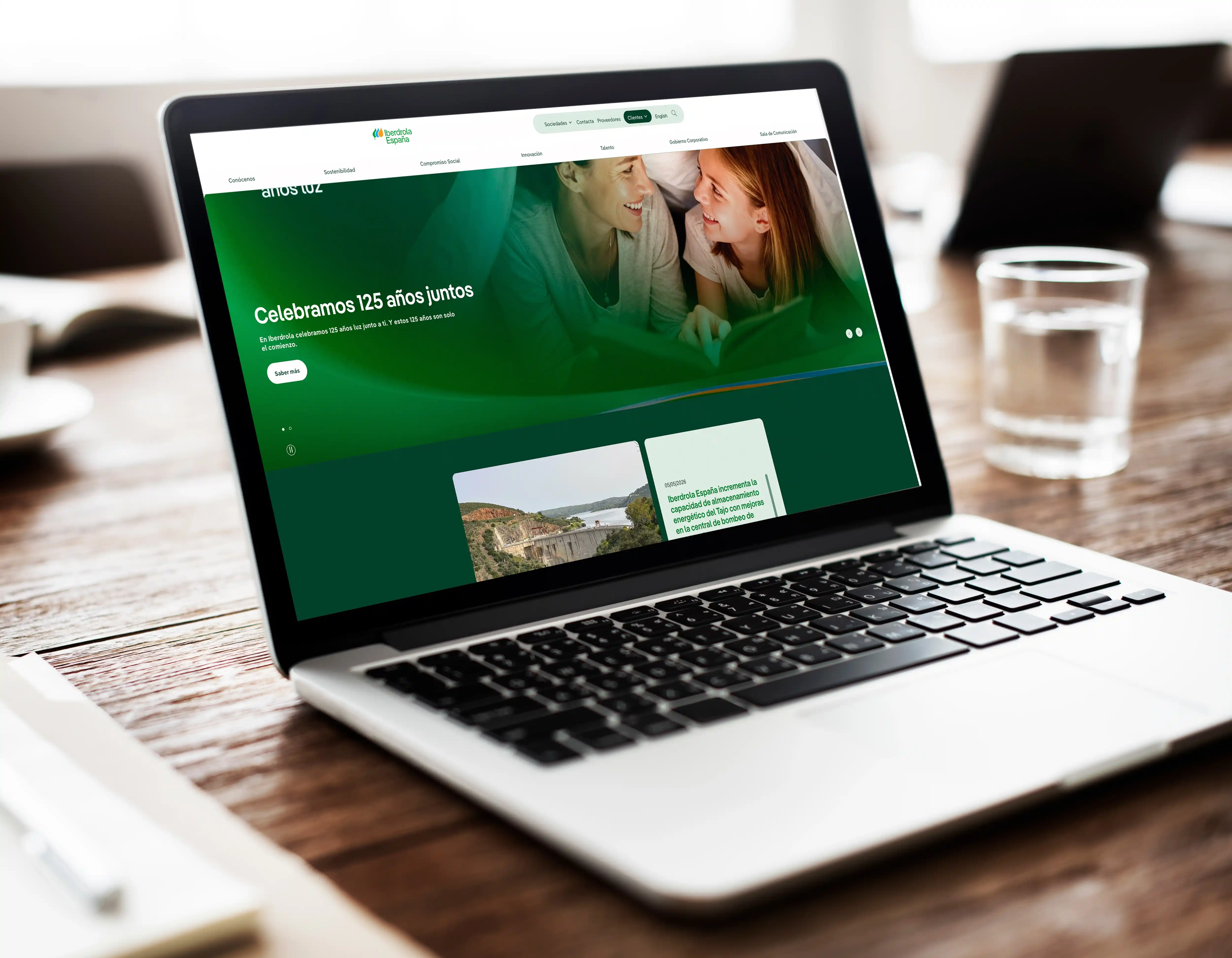 Laptop mostrando la web de Iberdrola España con taza de café y vaso de agua en la mesa.