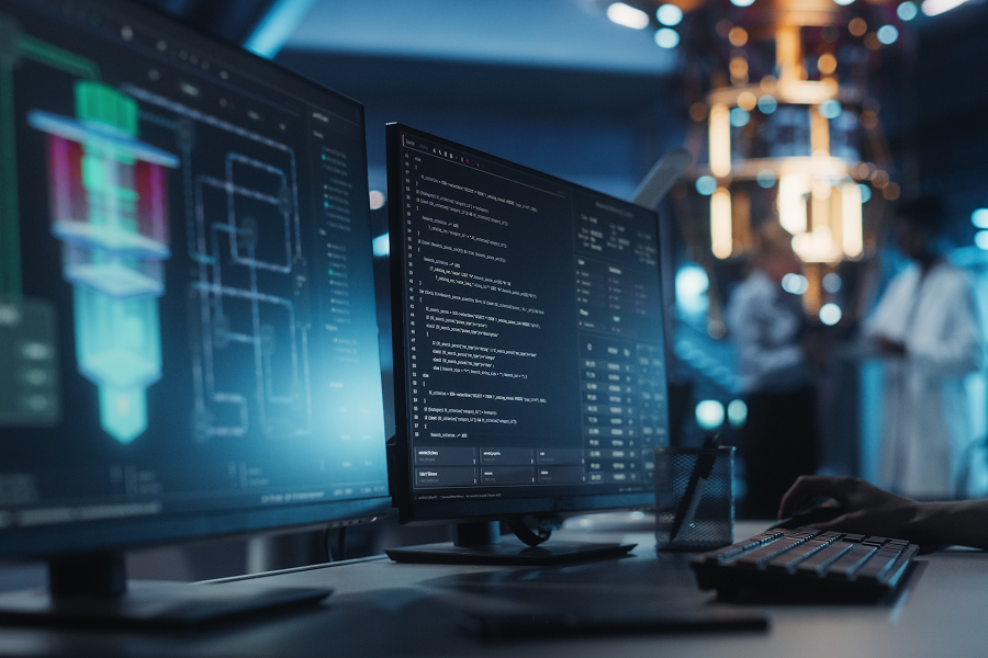 Computer screens displaying graphics and code, with a person working at the keyboard. In the background people can be seen in a high-tech laboratory setting.