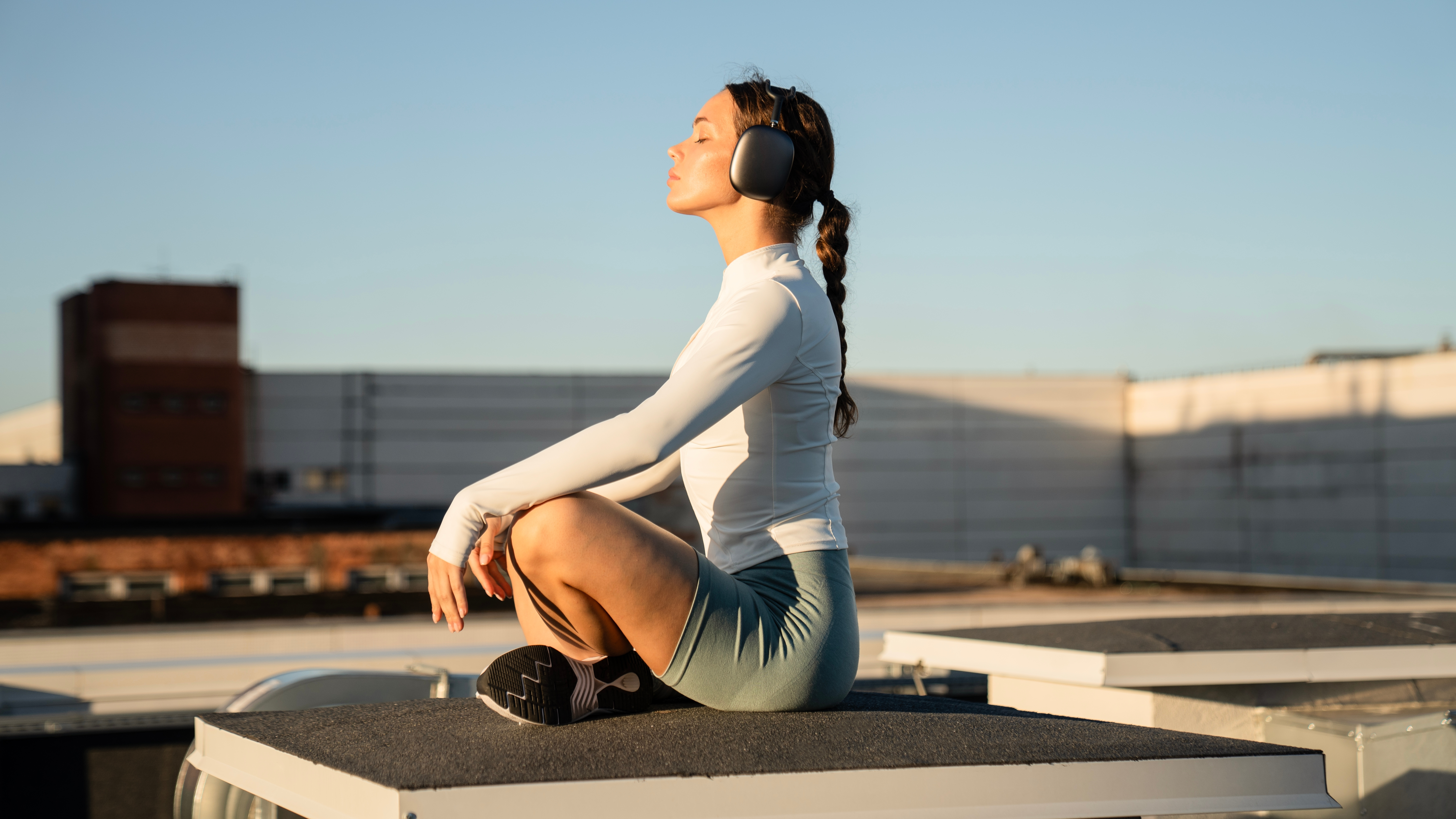 Woman meditating on a rooftop, wearing headphones, with sunlight illuminating her face.