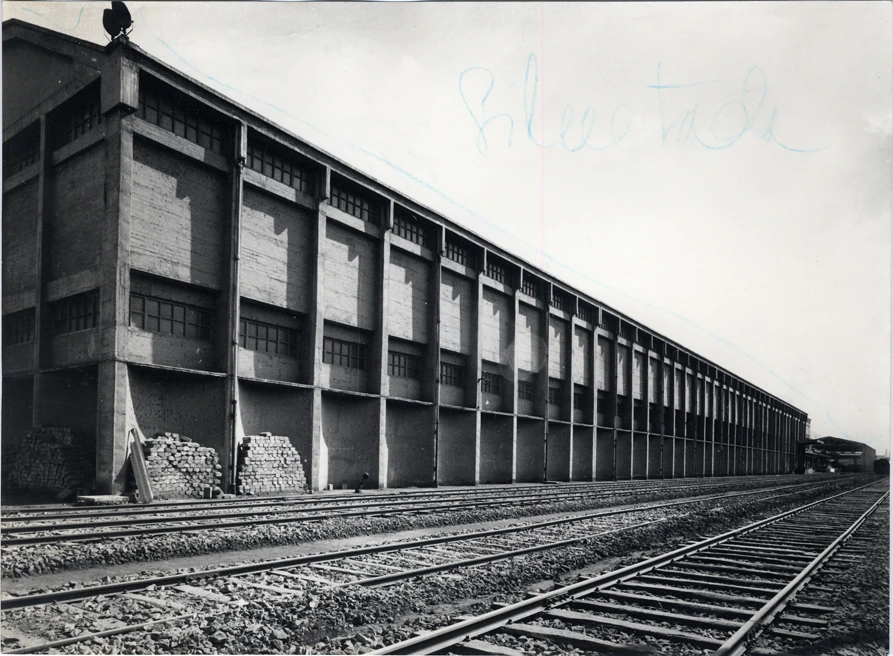 Side façade of a Nitrastur industrial building beside railway tracks in a historic photograph.