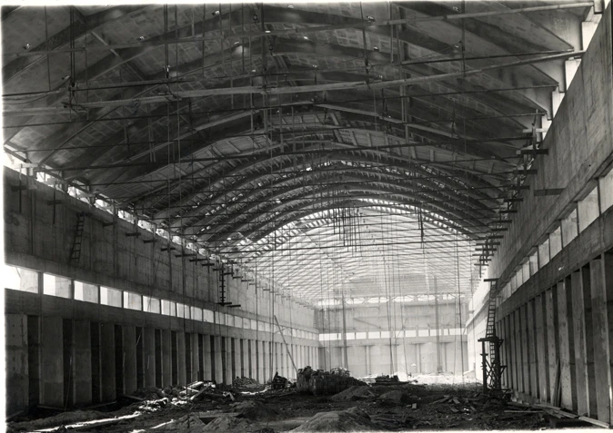 Historic photograph of the interior of a Nitrastur industrial building under construction, featuring an arched roof structure.
